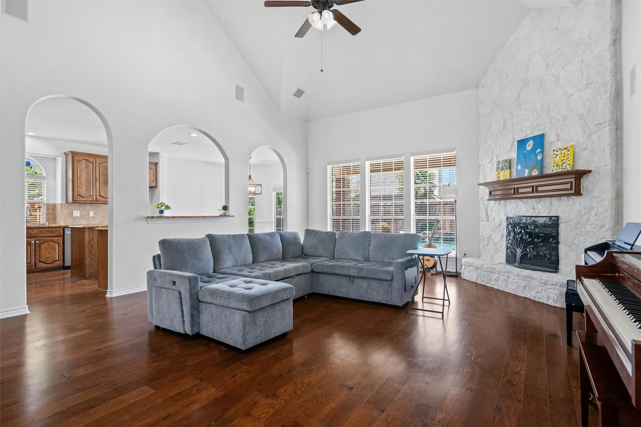 Vaulted ceiling, wood-finish flooring, white stone fireplace, multiple arched doorways, and a ceiling fan
