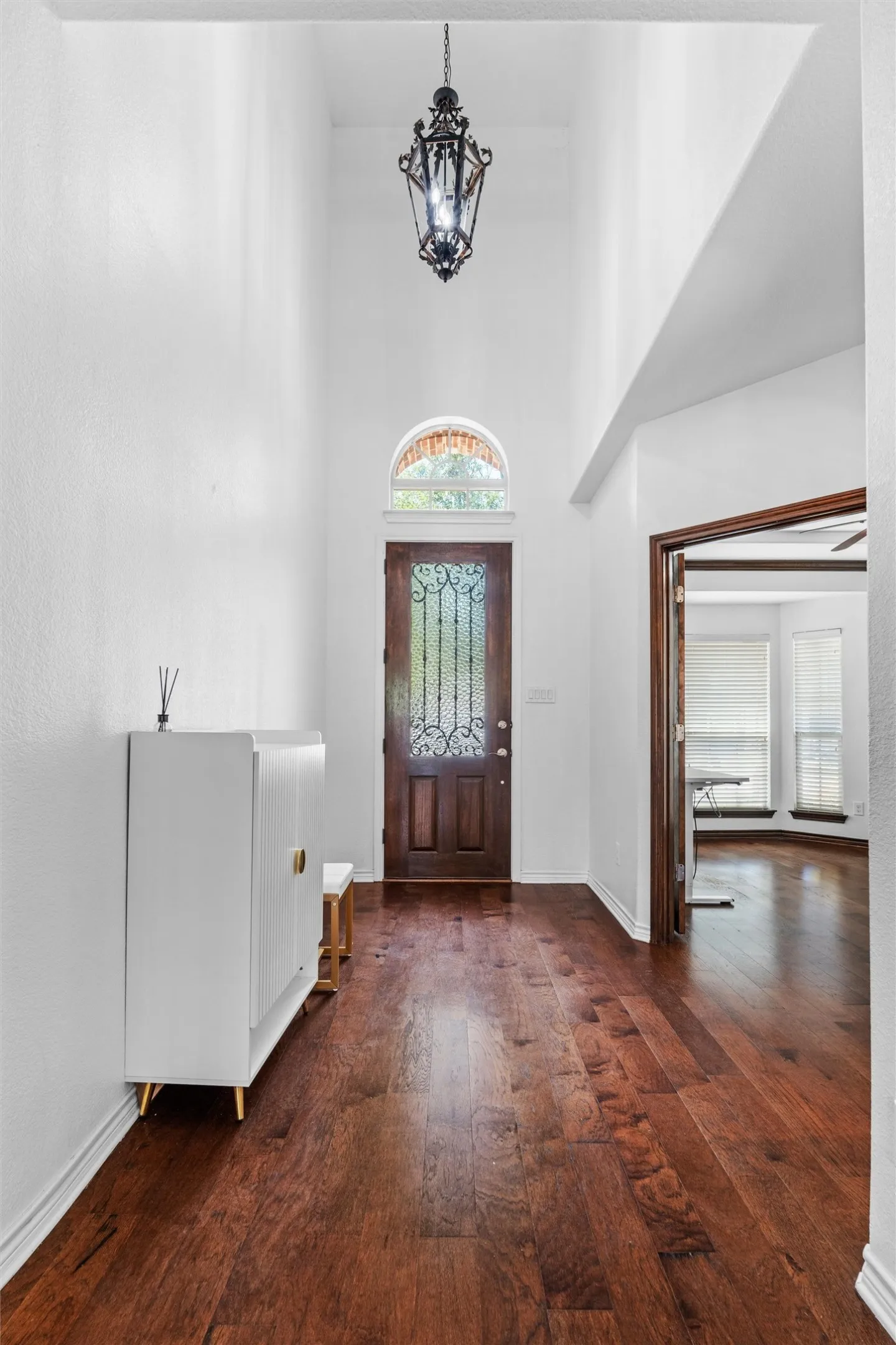 Expansive entryway featuring high ceilings, dark wood-finish flooring, an arched transom window, a dark wood entry door with decorative ironwork, and an ornate hanging light fixture