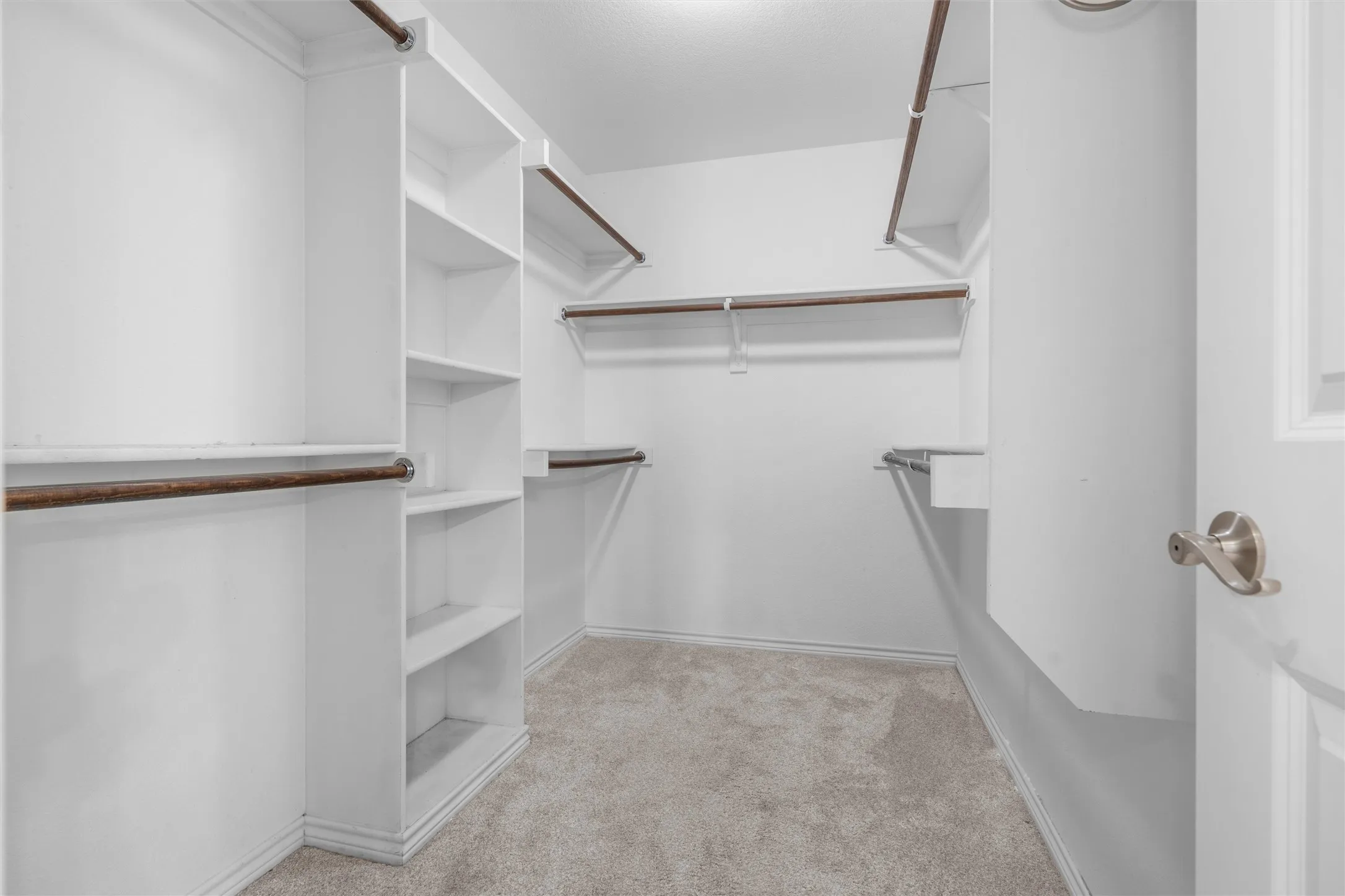 Built-in shelving, multiple hanging rods, and neutral carpet flooring