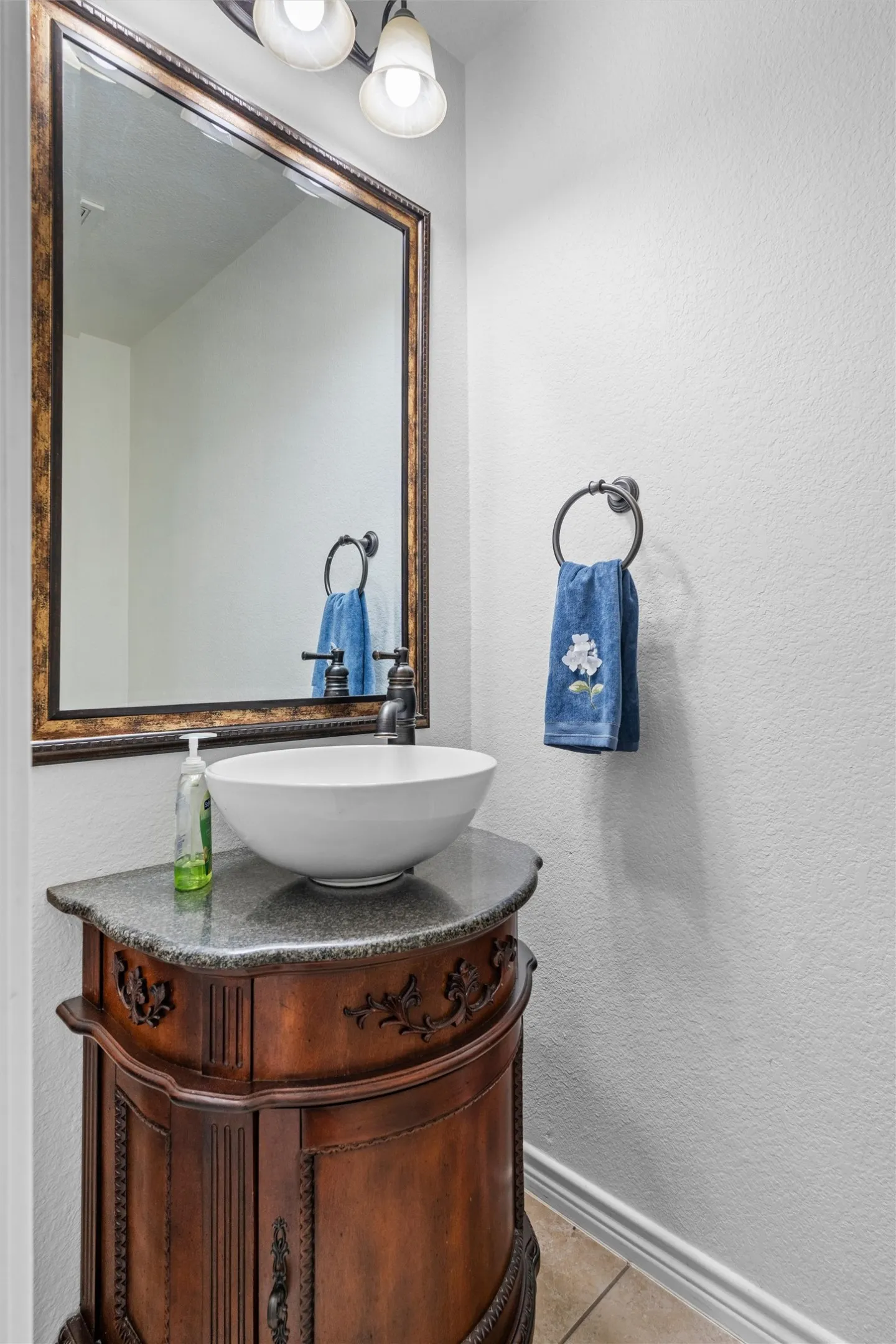 Ornate wood vanity with a vessel sink, textured countertop, and framed mirror