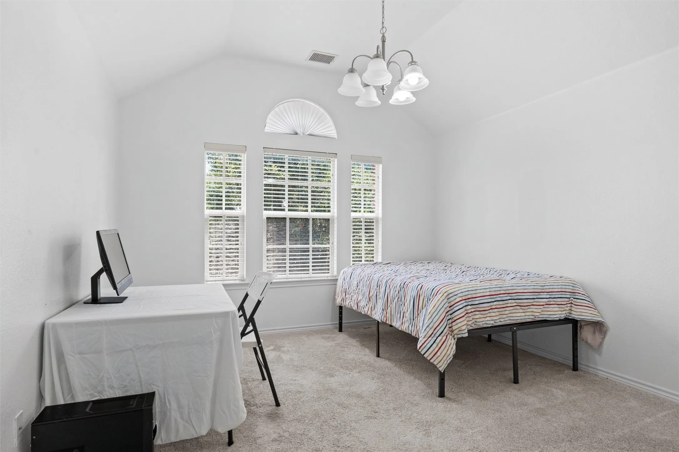 Vaulted ceiling with a chandelier, arched window, two vertical windows with blinds, and light-toned carpeting