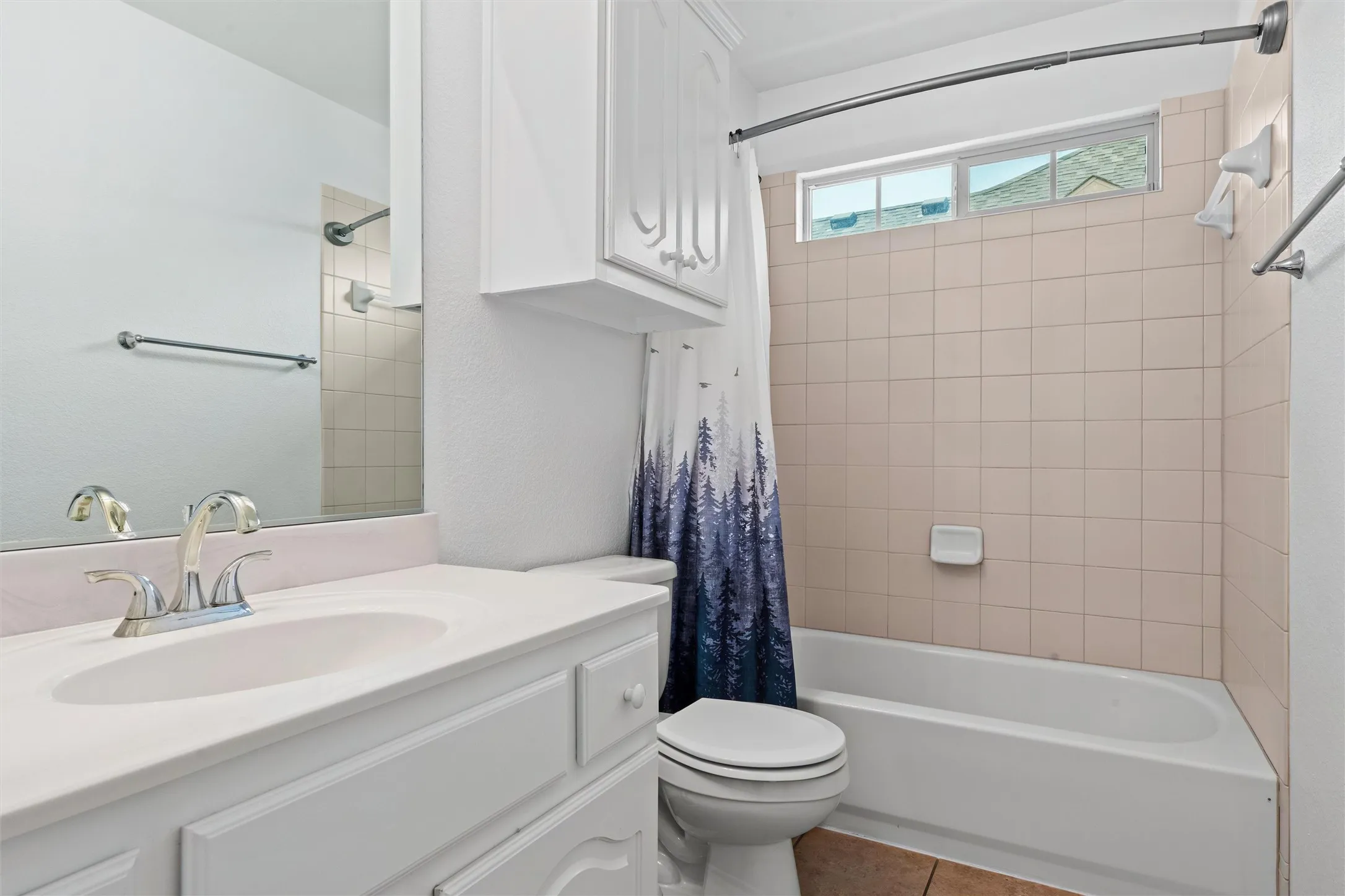 Clean and functional bathroom featuring a double vanity with white cabinetry and dual sinks, ceramic tile flooring, and an alcove bathtub with shower surround and glass enclosure