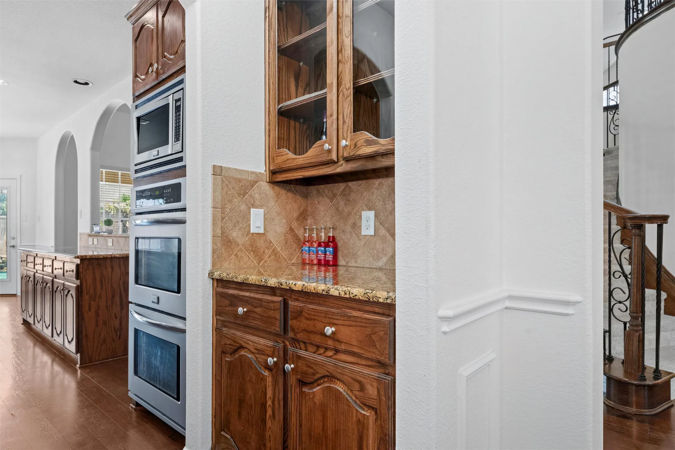 Built-in double ovens, microwave, and rich wood cabinetry with glass fronts