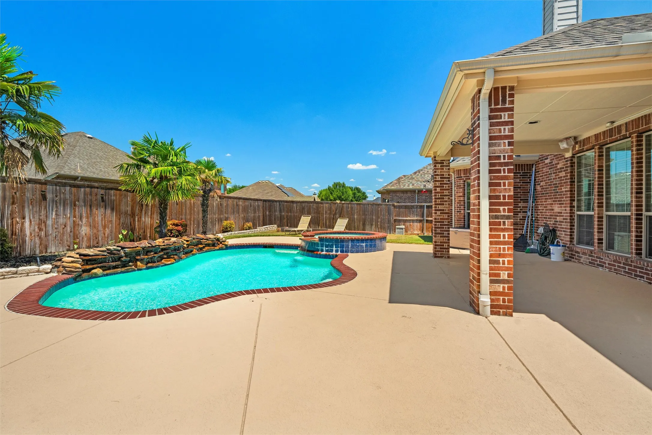 Expansive backyard featuring a freeform pool with integrated spa, stone waterfall, and mature palm trees