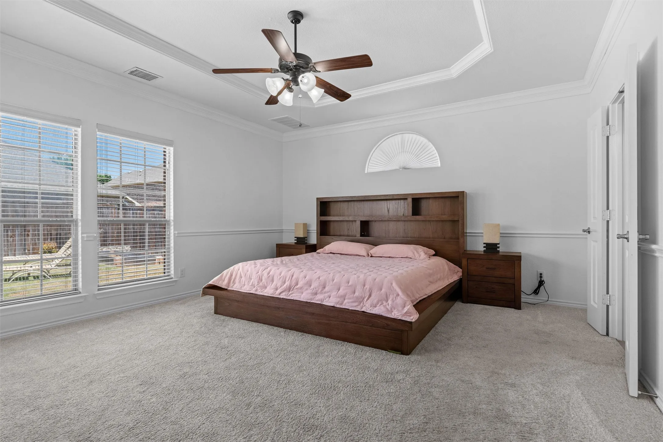 Tray ceiling with crown molding, ceiling fan, two large windows, chair rail molding, and carpeted flooring