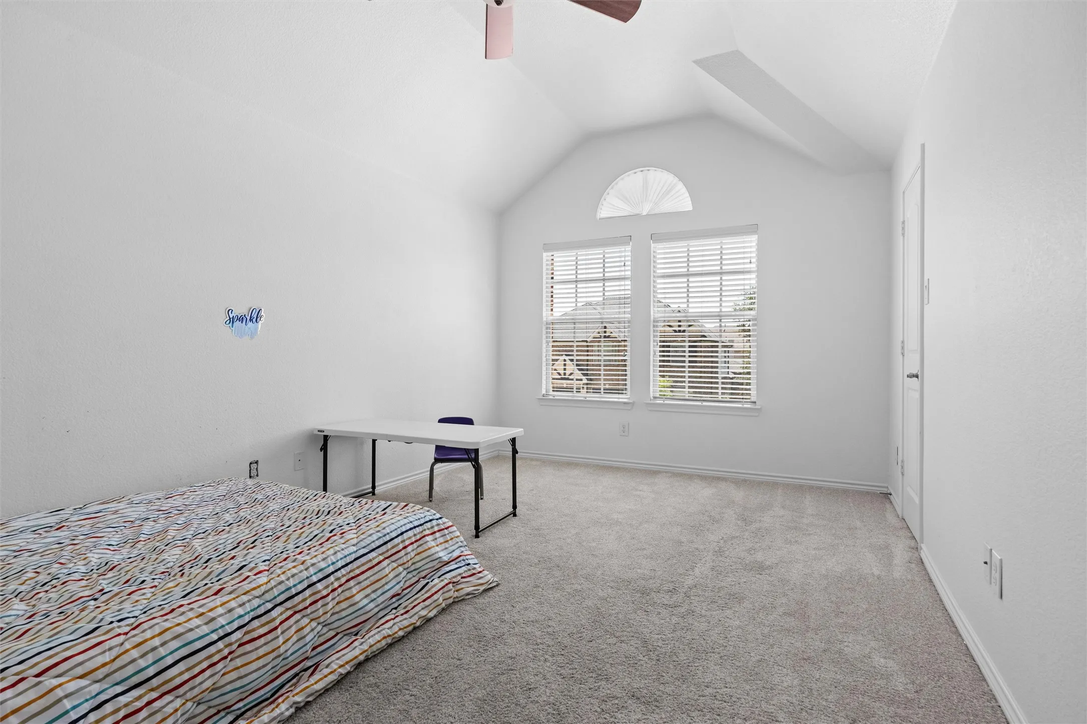Vaulted ceiling room featuring carpet flooring, dual windows with blinds, an arched transom window, and a ceiling fan