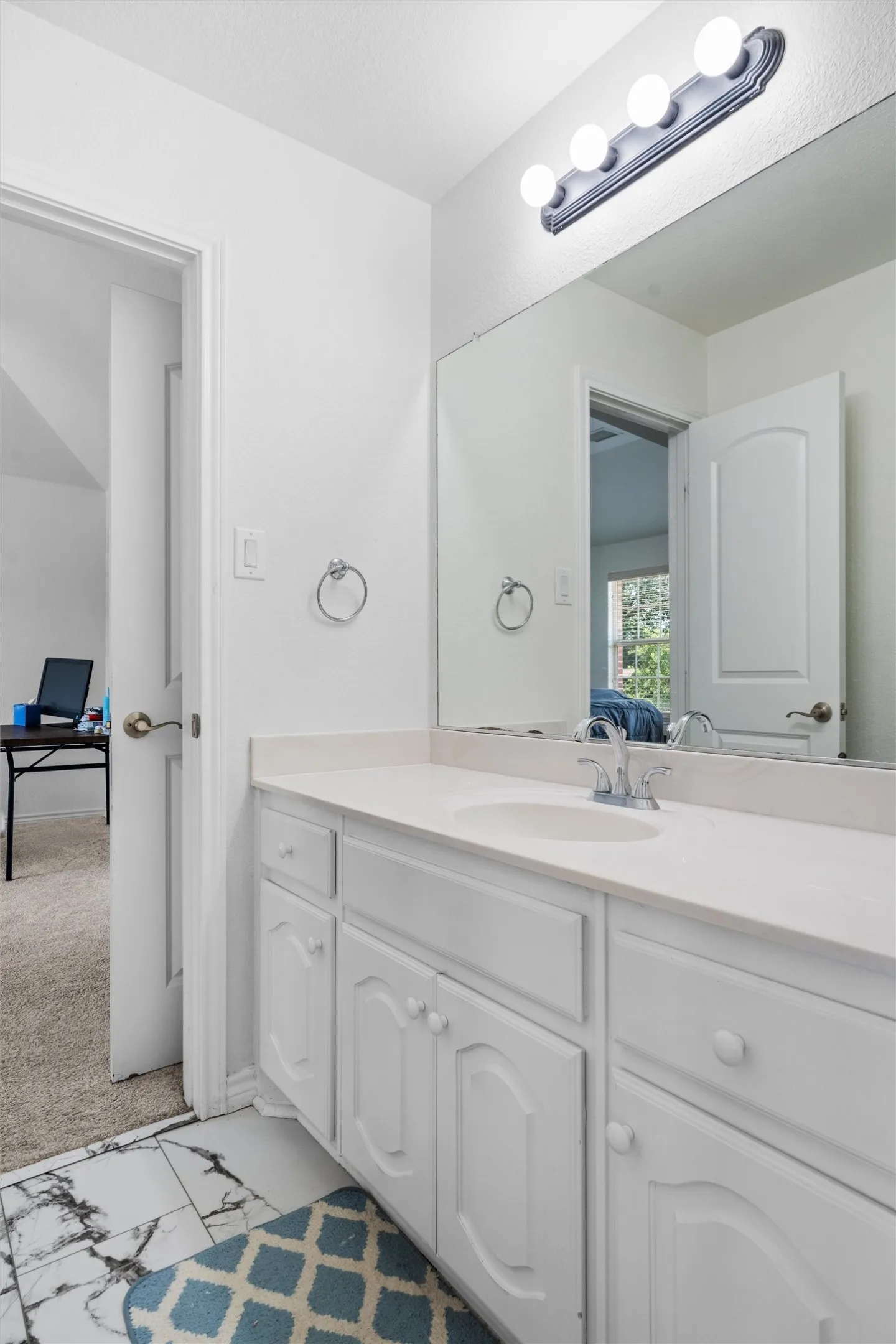 White vanity with integrated sink, light countertop, surface-mounted mirror, and four-bulb vanity lighting fixture