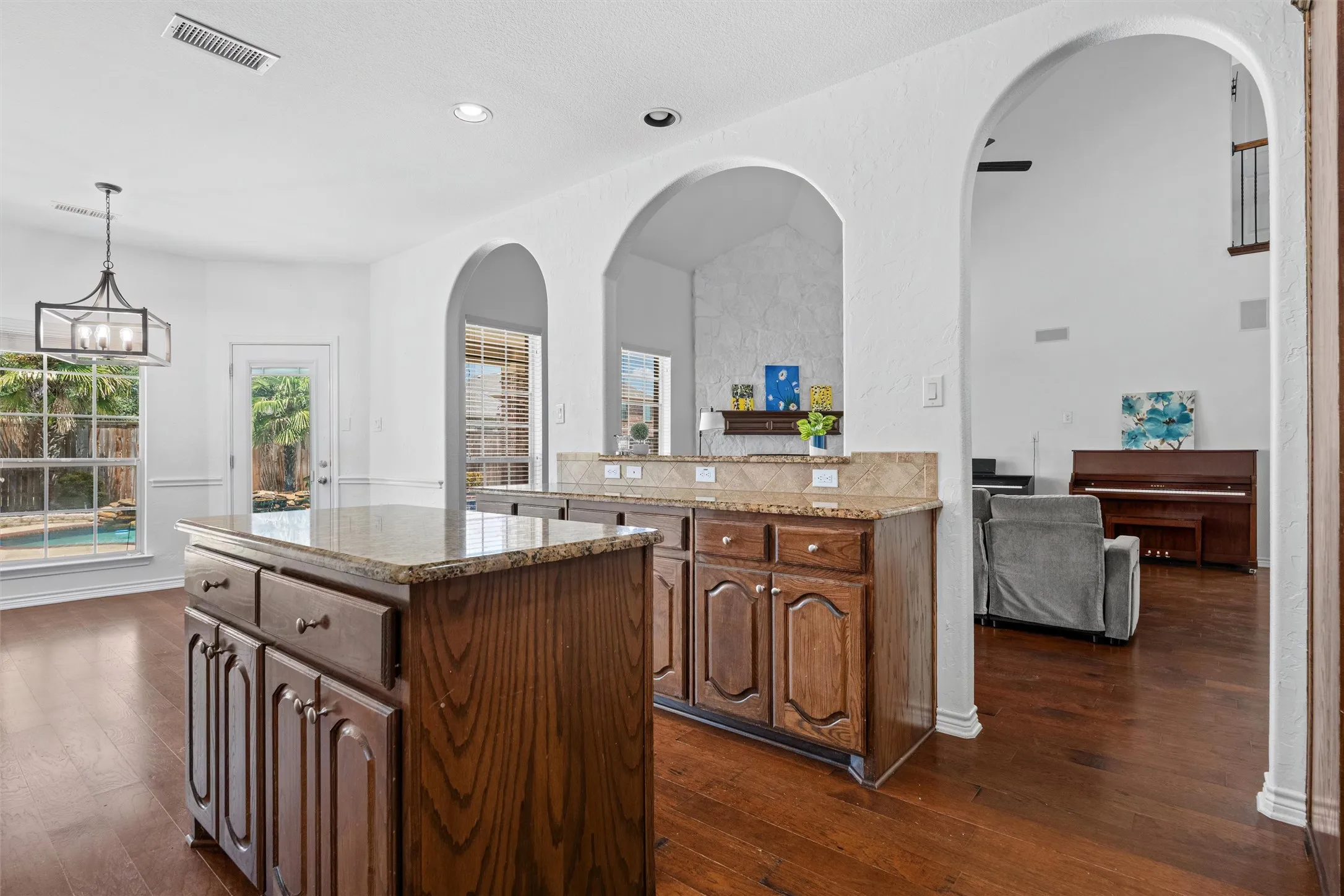 Wood-finish flooring throughout, kitchen island with stone countertop, built-in cabinetry, multiple arched entries, and a geometric-frame chandelier