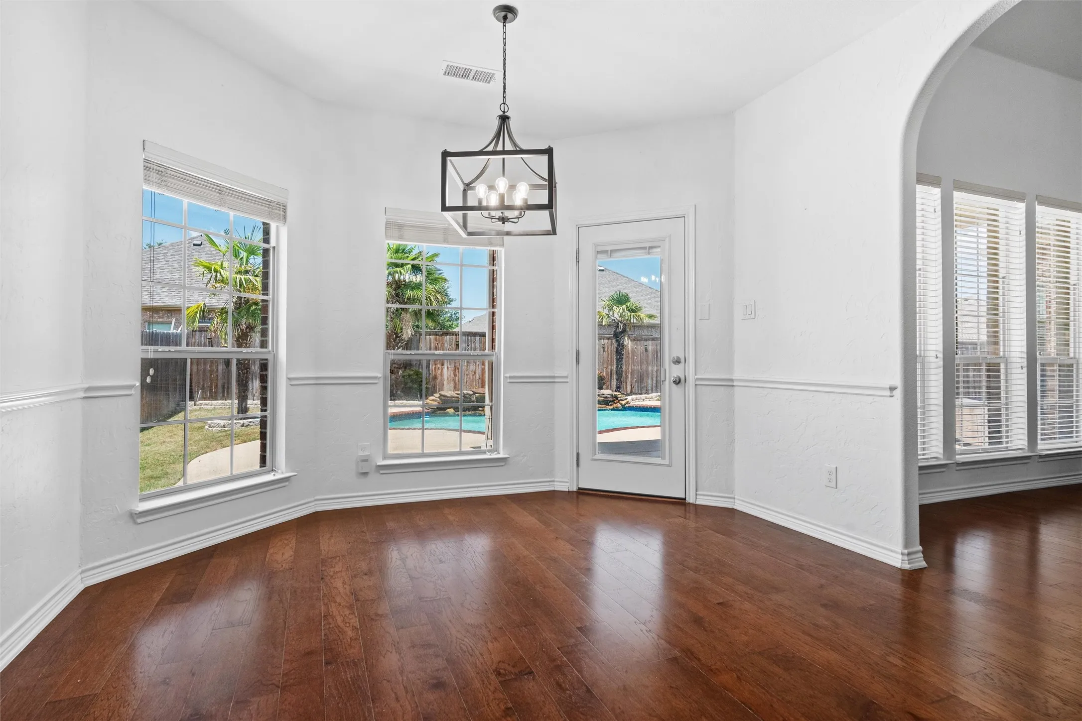 Hardwood-finish flooring, white walls with wainscoting, an arched doorway, and a contemporary chandelier