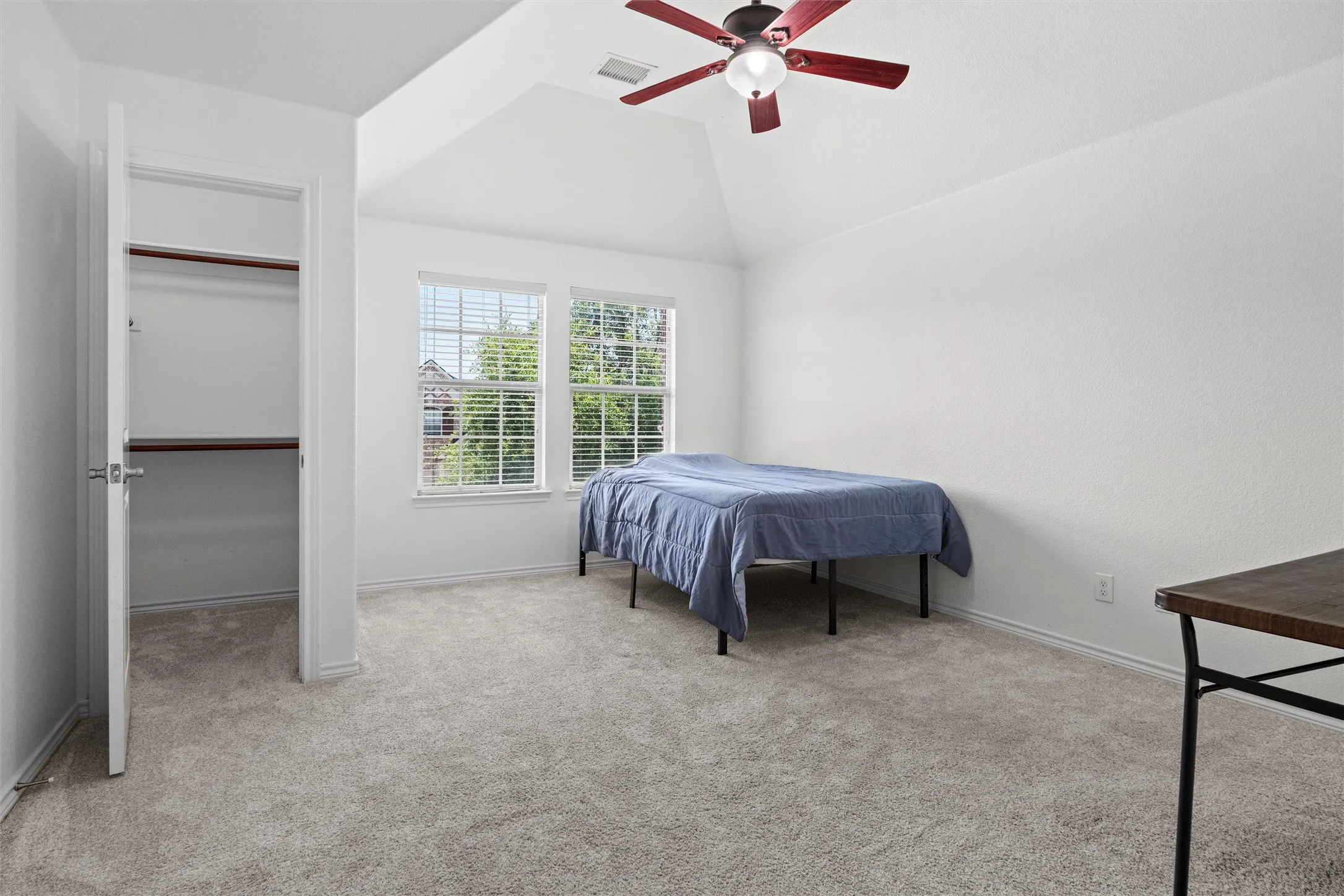 Vaulted ceiling with a ceiling fan, plush gray carpeting, dual windows with blinds, and a built-in closet with shelving