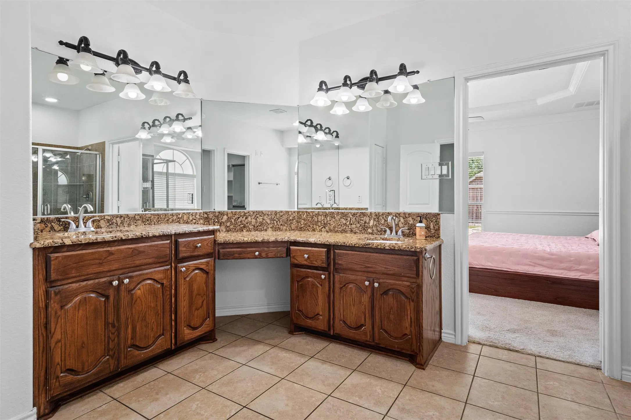 Dual sink vanity with granite-finish countertops, warm wood-finish cabinetry, and tiled flooring