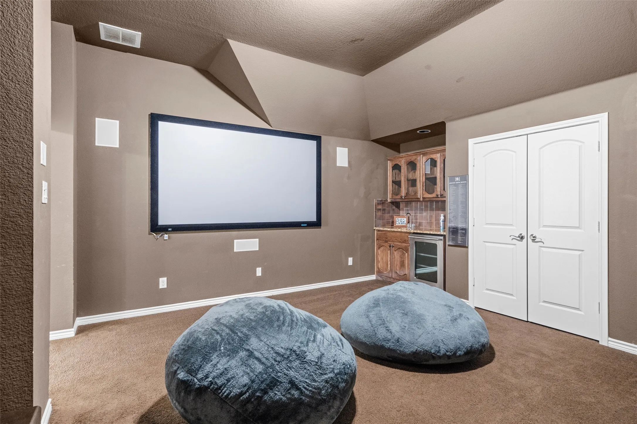 Integrated projector screen, built-in speaker system, vaulted ceiling, wet bar with wood cabinetry, and double white paneled doors