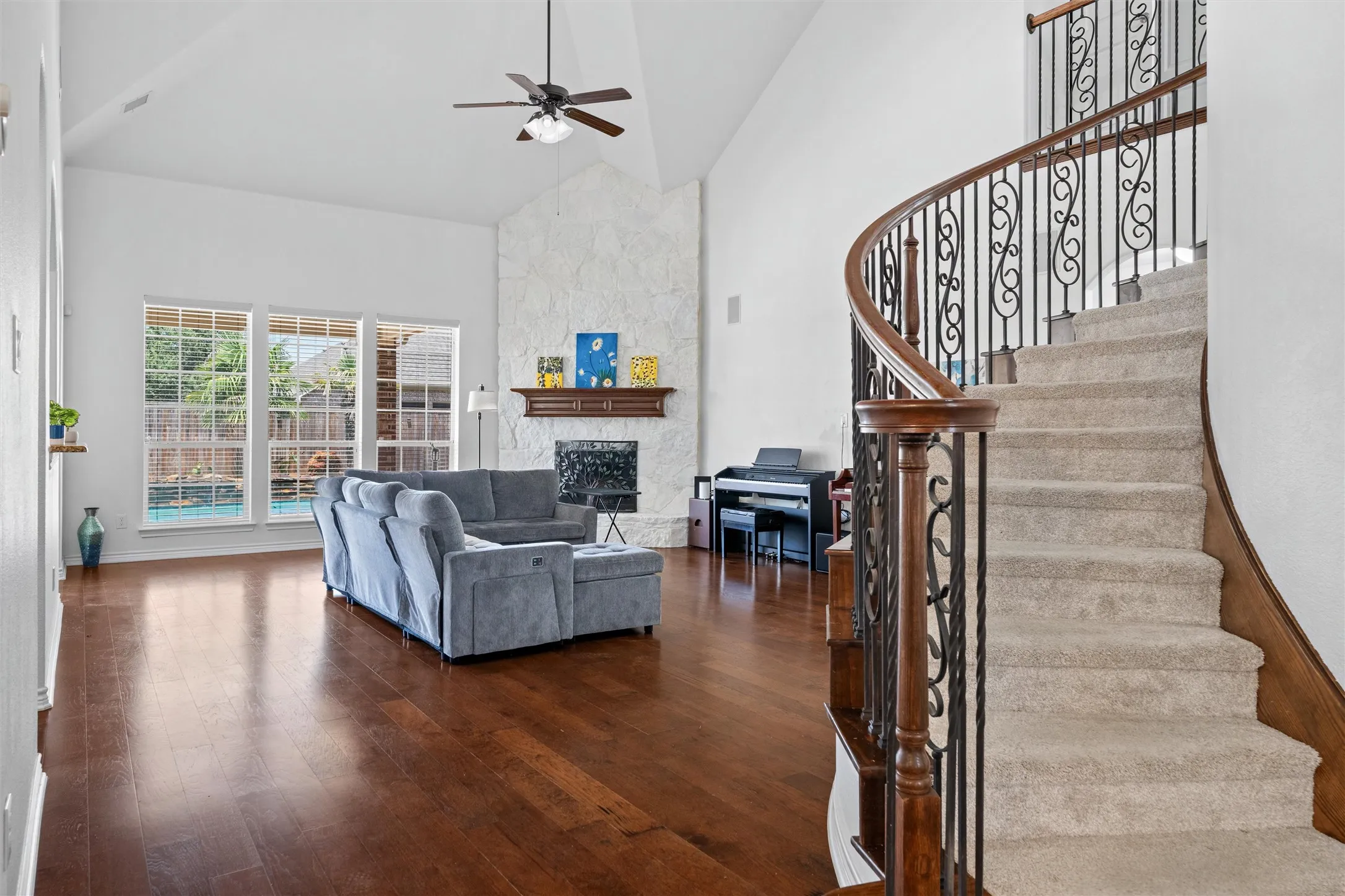 Spacious living area featuring high vaulted ceilings, wood-finish flooring, and a stone-clad fireplace
