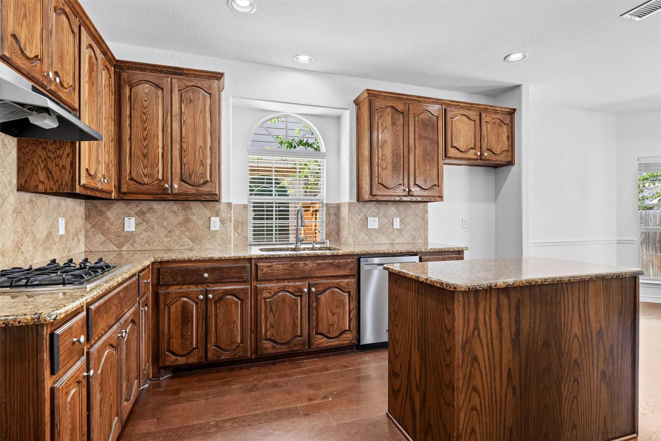 Kitchen featuring wood-finish cabinetry, granite countertops, tile backsplash, built-in gas range, and a central island