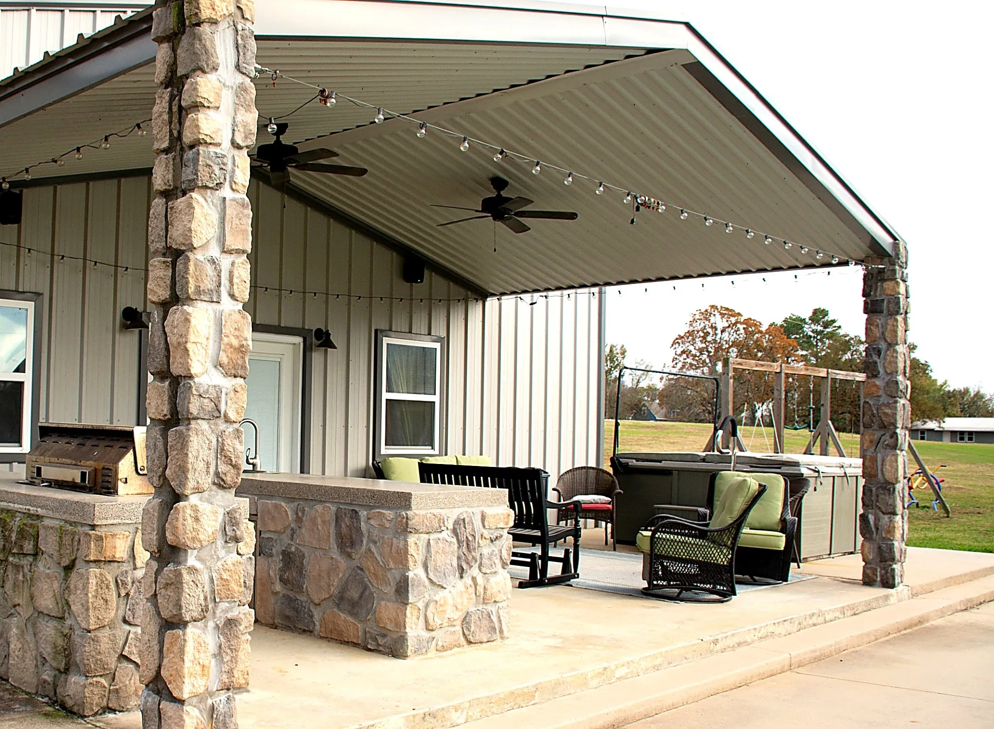 Covered concrete patio with stone pillars, featuring an outdoor kitchen
