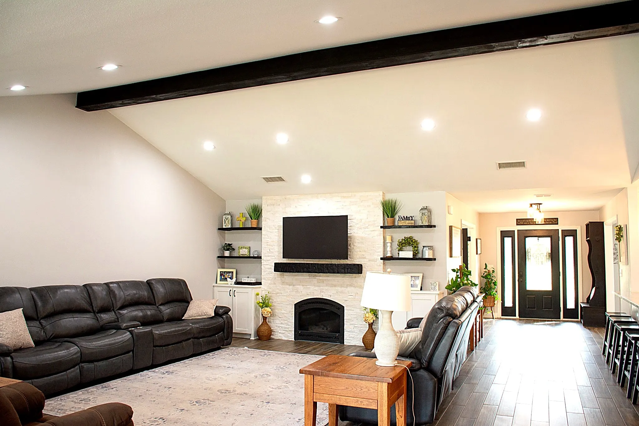 Family room, vaulted ceiling with beam, recessed lighting, fireplace with stone surround, and built-in shelving
