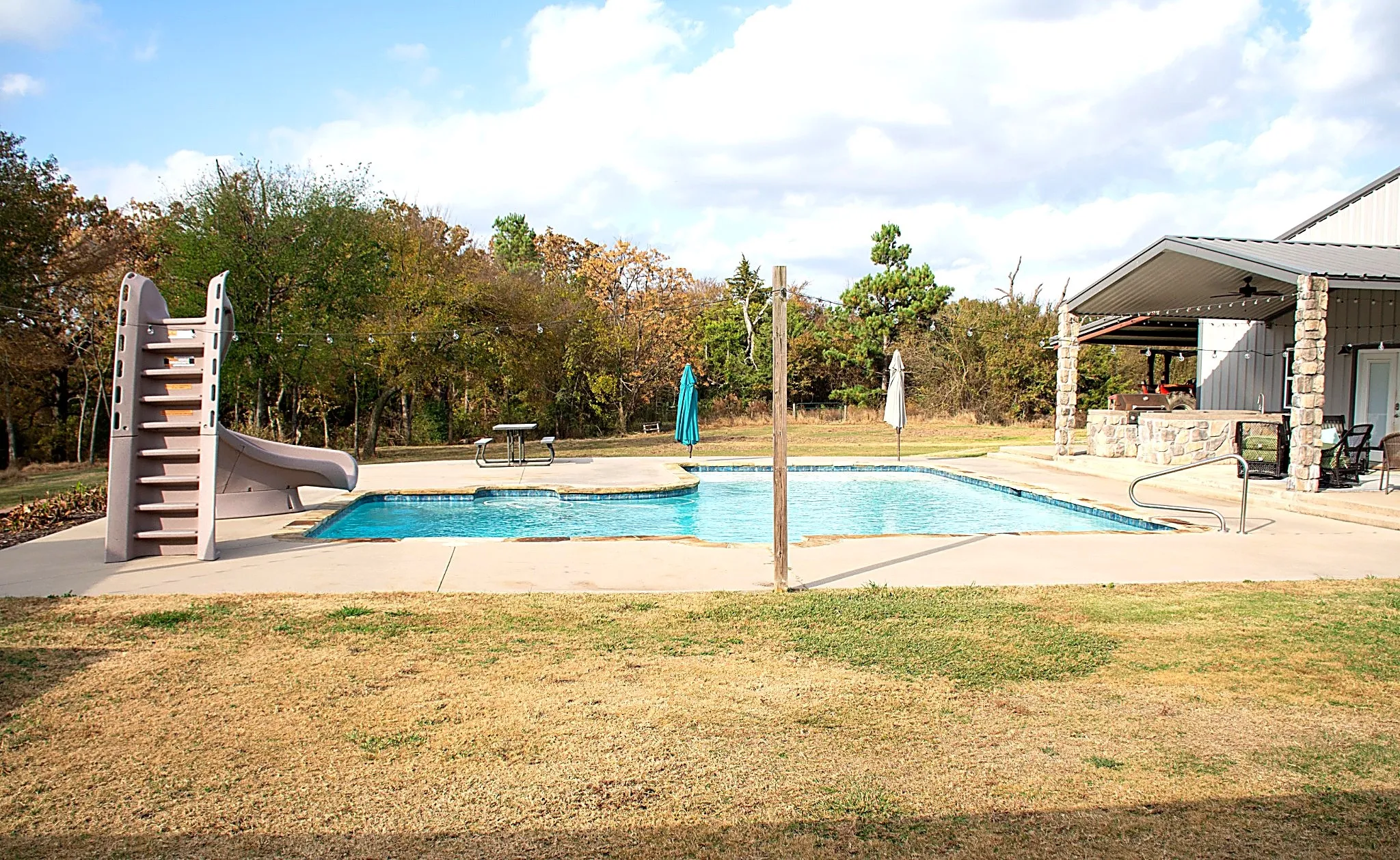 Outdoor swimming pool with concrete decking, a pool slide, and adjacent covered patio
