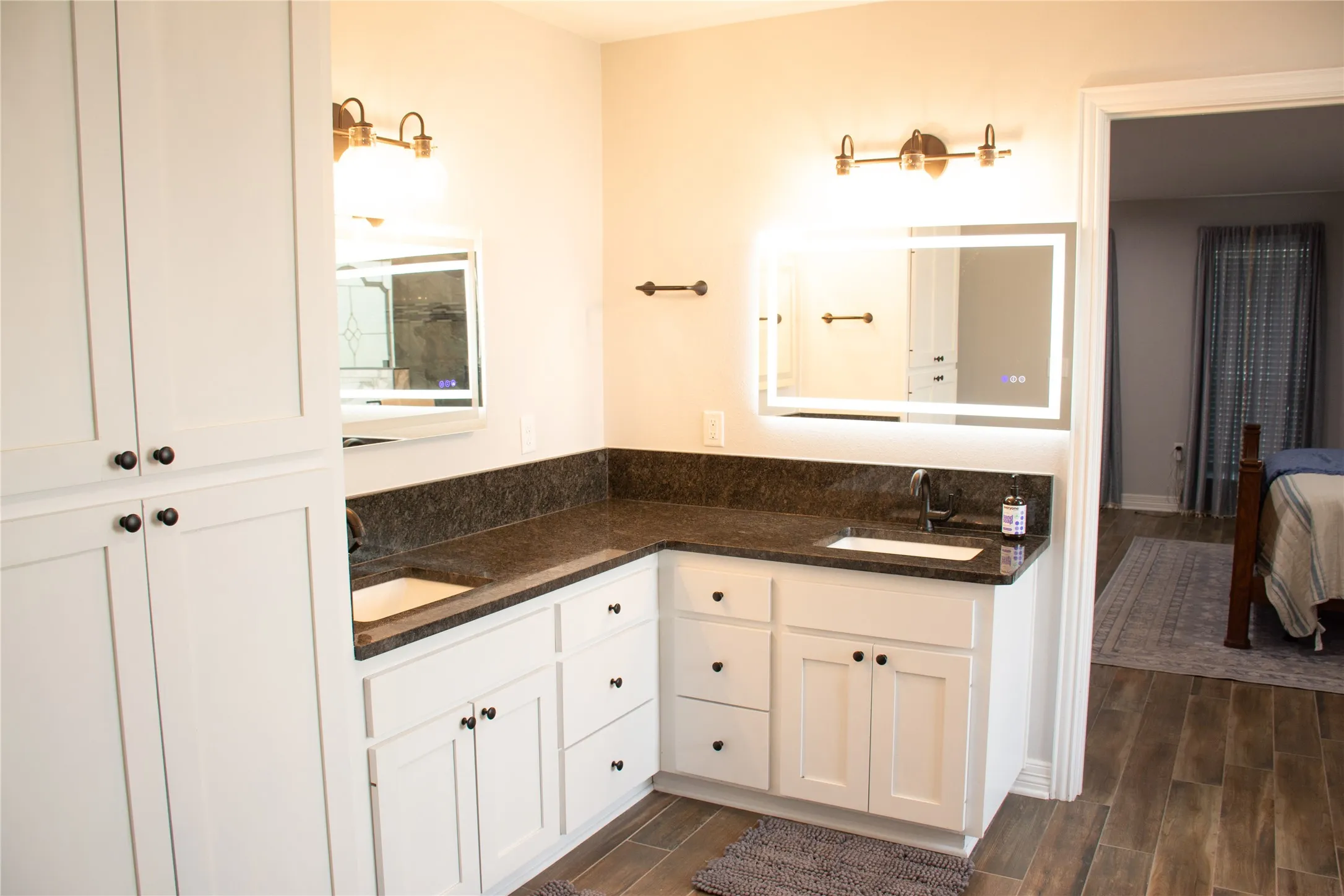 Double vanity with white cabinetry, integrated sinks, illuminated mirrors