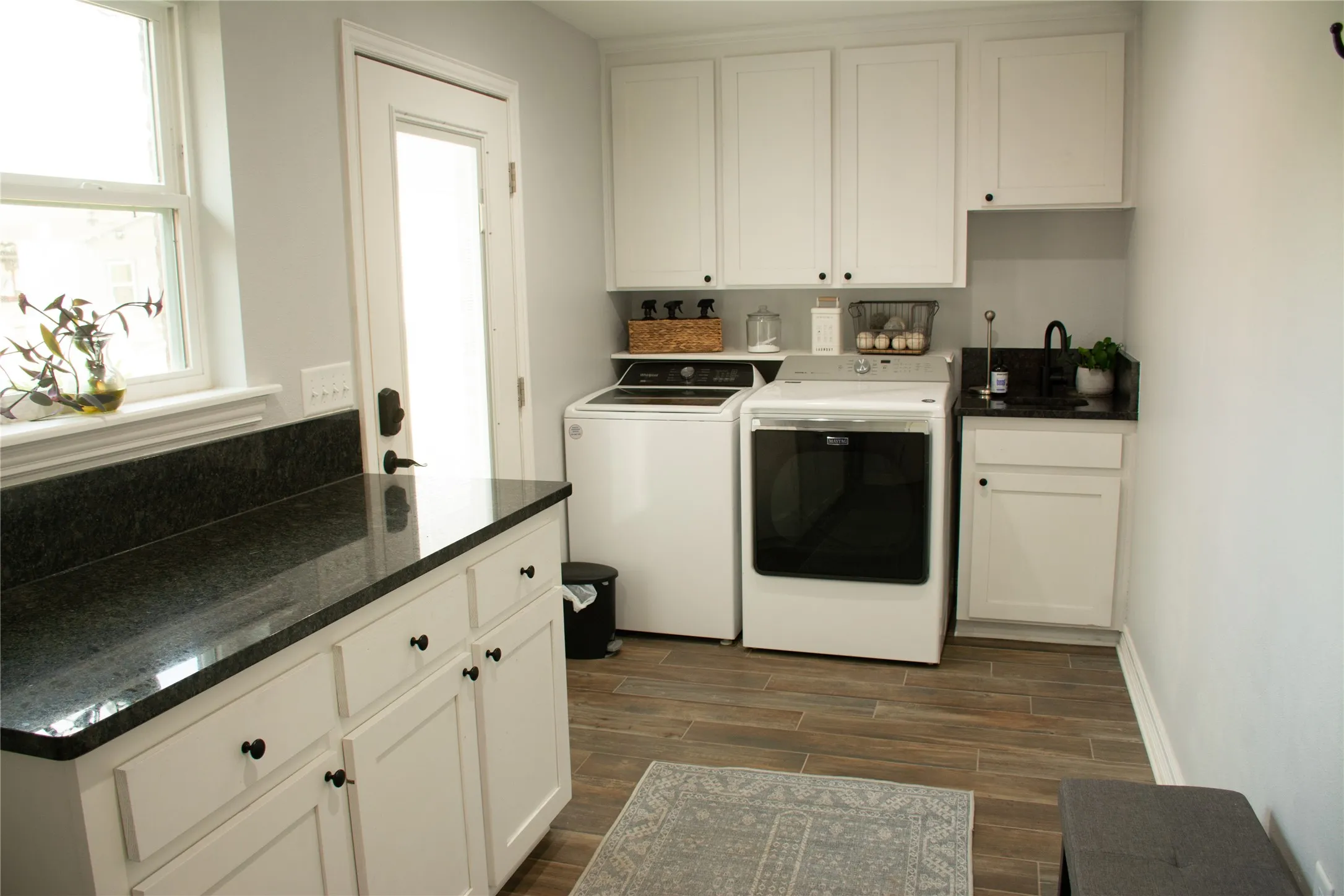 White shaker-style cabinetry, granite countertops, a utility sink, window and back door, room for a freezer