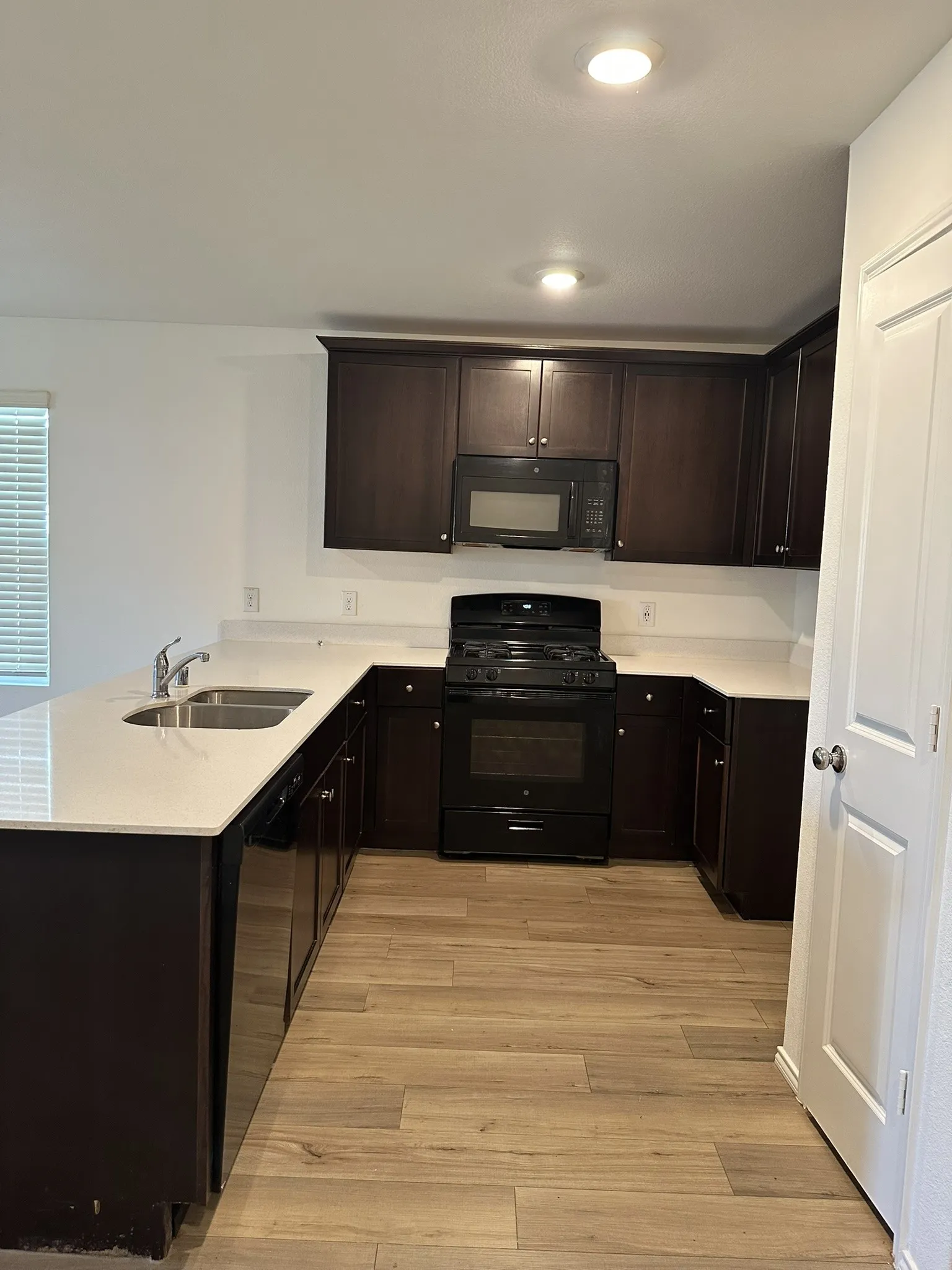 Kitchen featuring black appliances, a peninsula, light countertops, light wood-style flooring, and dark brown cabinetry