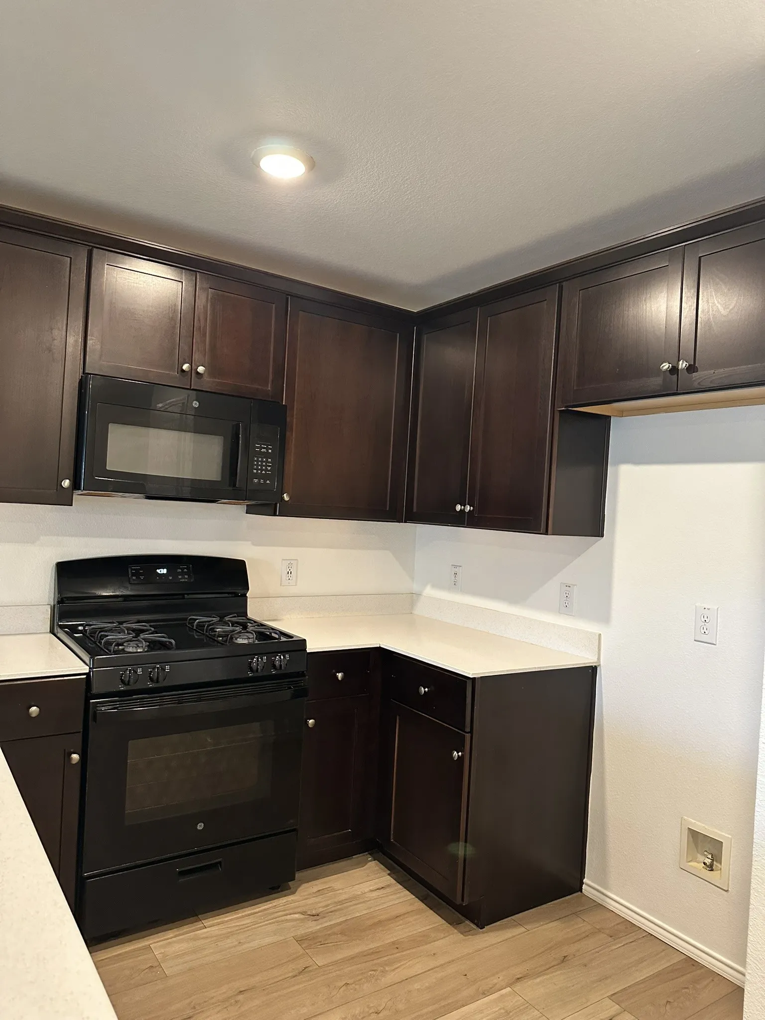 Kitchen with black appliances, light countertops, dark brown cabinets, and light wood-style flooring