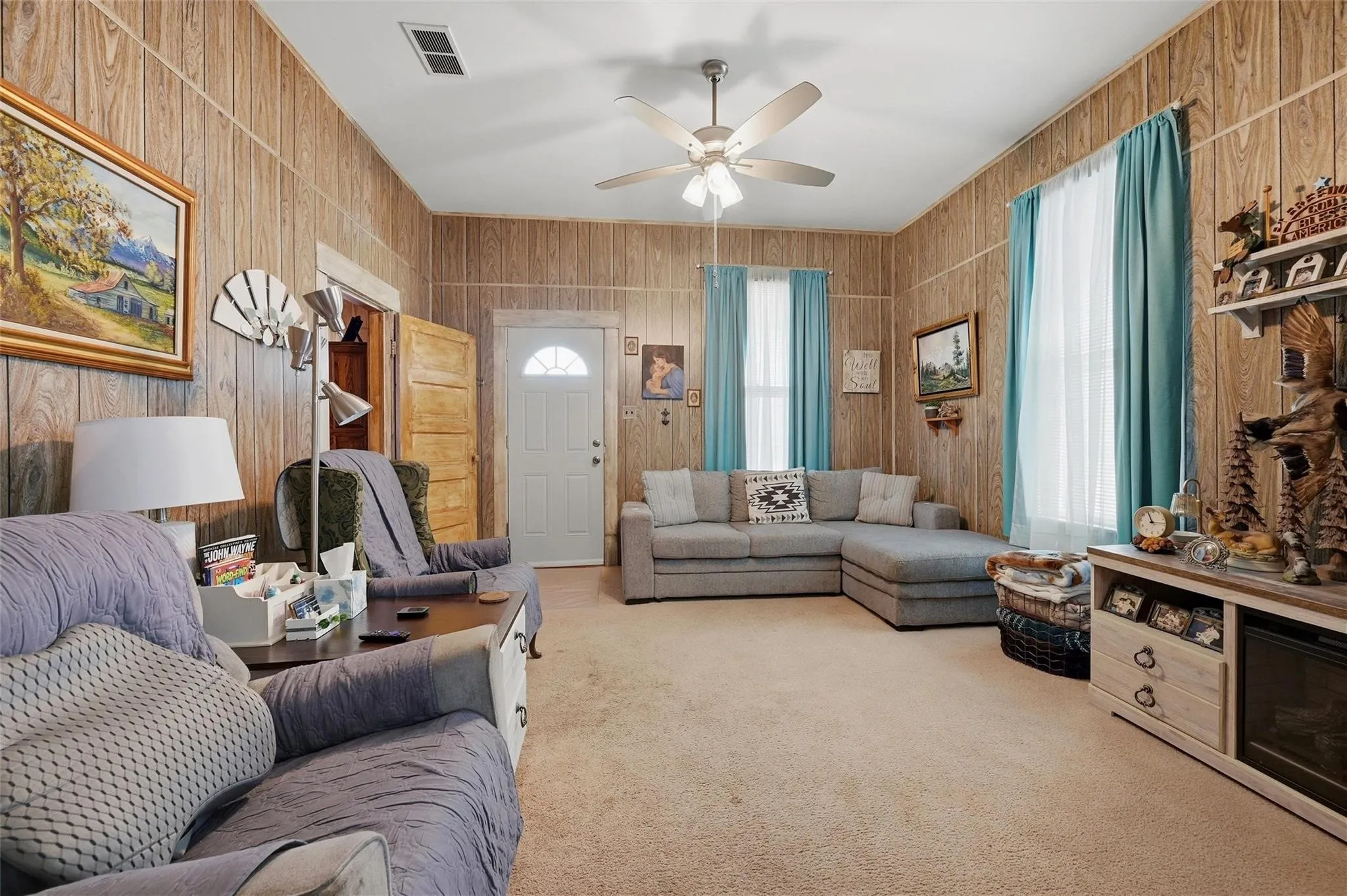 Carpeted flooring, paneled walls, ceiling fan with light fixture, and a white entrance door with an arched window