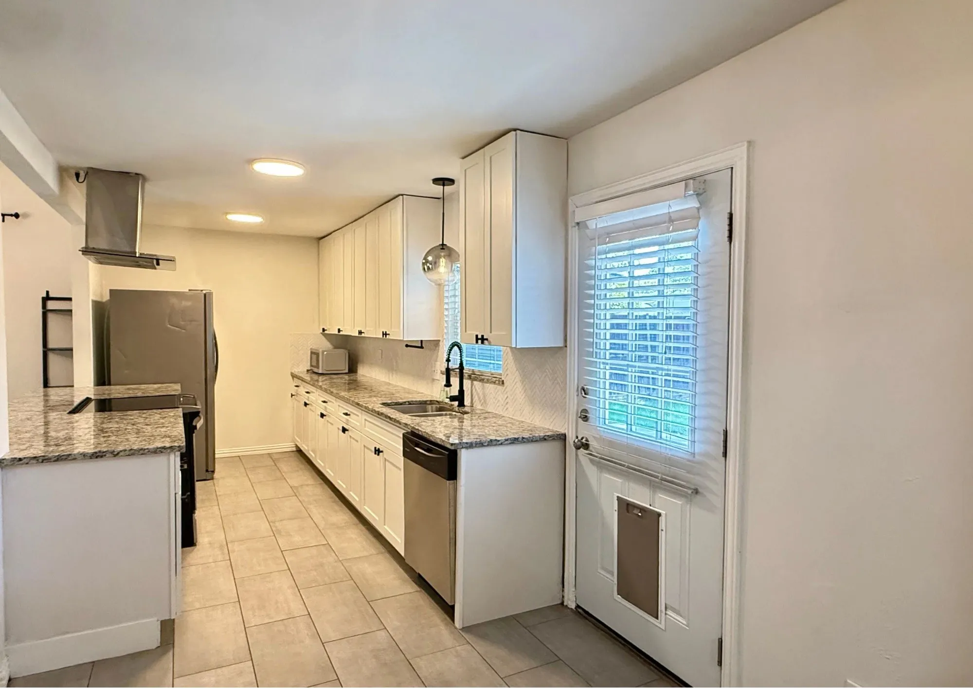 Modern kitchen featuring white cabinetry, light-toned granite countertops, stainless steel appliances, and tile flooring