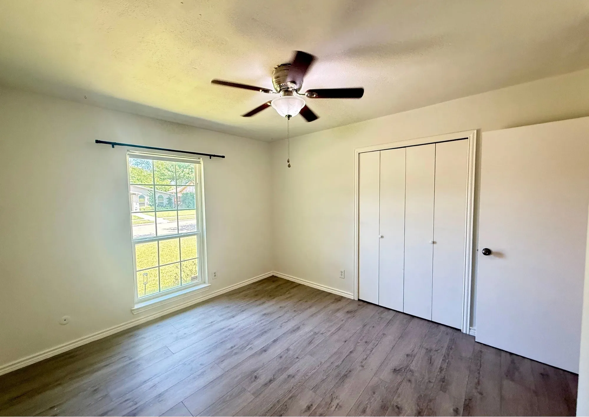 Wood-finish flooring, ceiling fan with light fixture, double-pane window, and white bi-fold closet doors