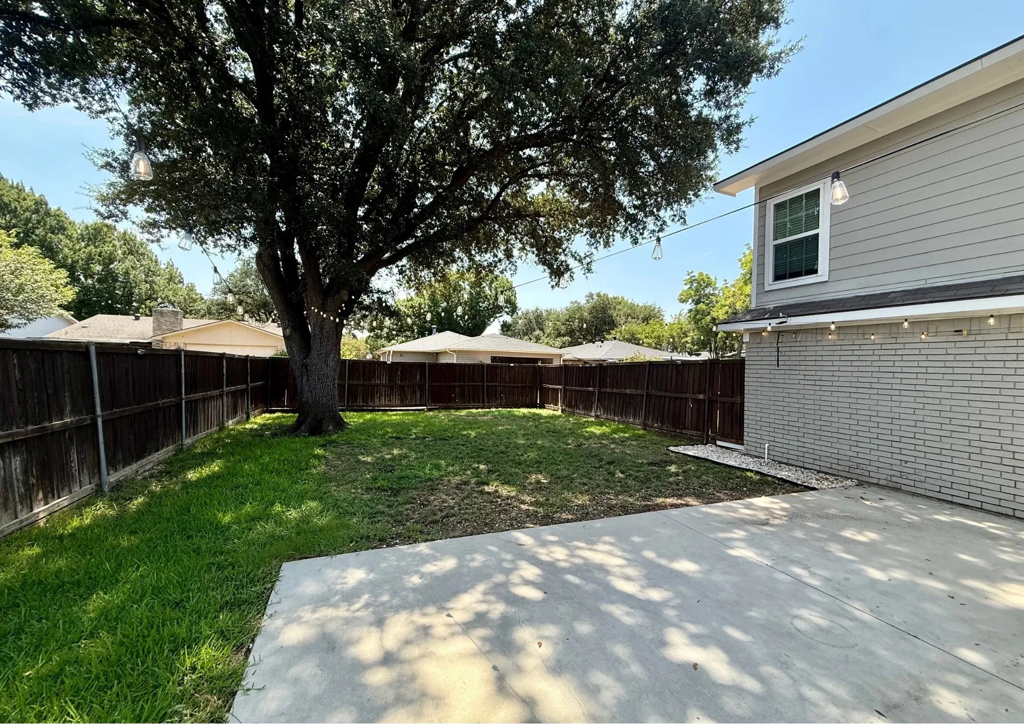 Expansive backyard featuring a mature tree, wood privacy fencing, and a concrete patio