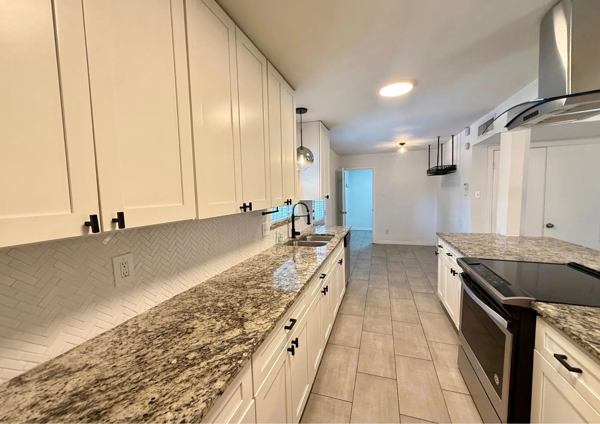 White shaker cabinetry with black hardware, patterned tile backsplash, stone countertops, and stainless steel appliances