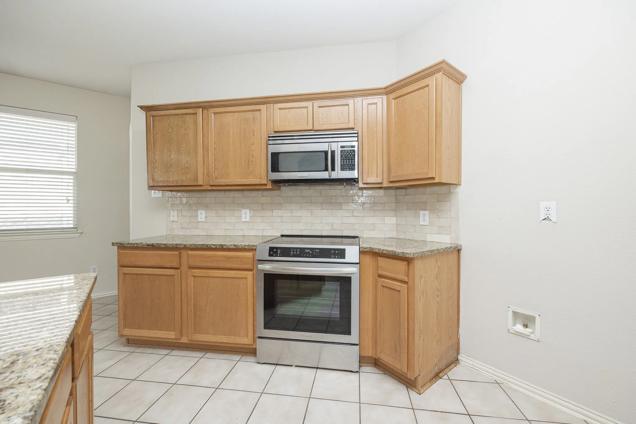 Kitchen featuring wood cabinetry, stainless steel microwave, stainless steel range, patterned tile backsplash, and light-toned countertops