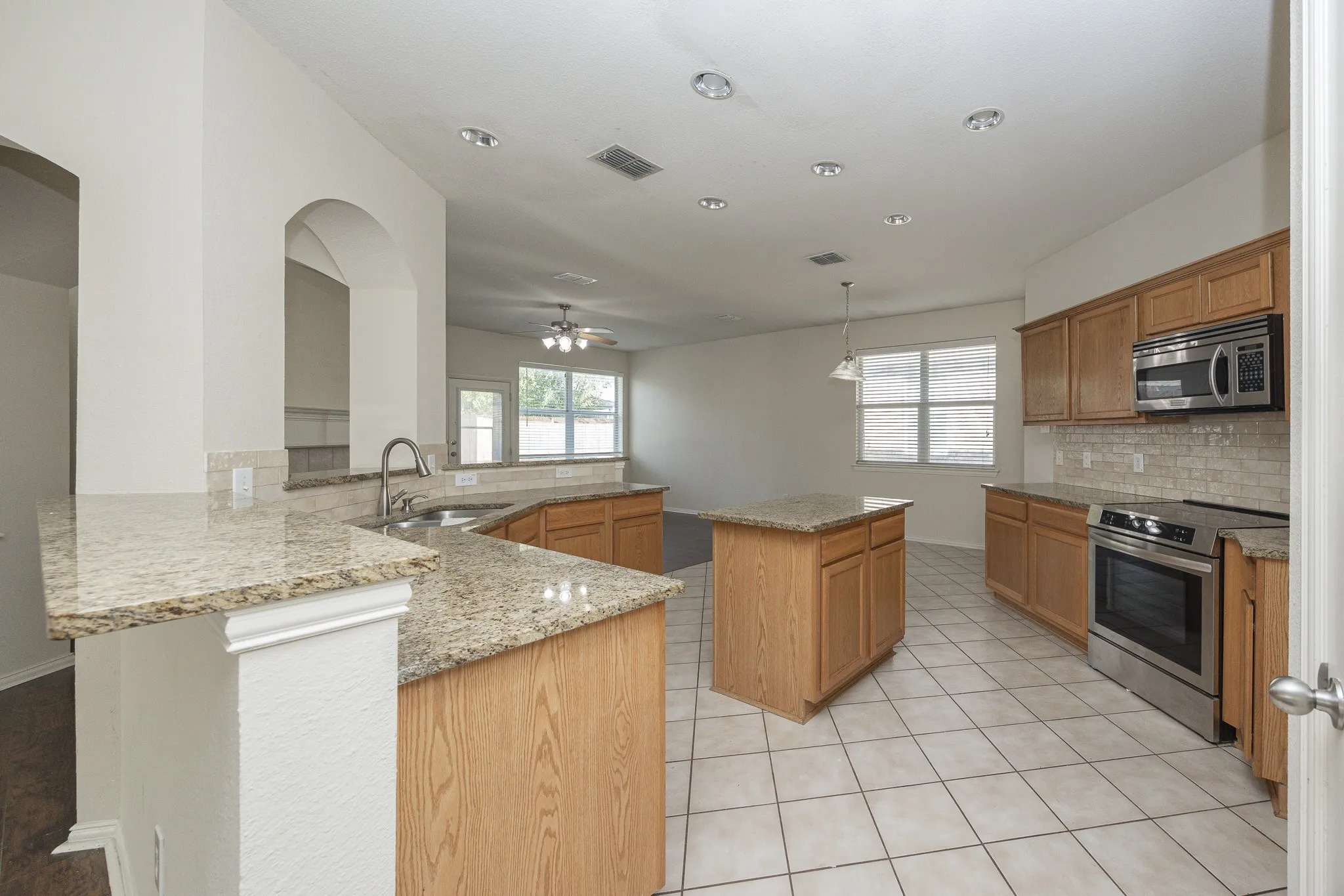 Kitchen featuring tile flooring, wood cabinetry, stone countertops, stainless steel appliances, and recessed lighting