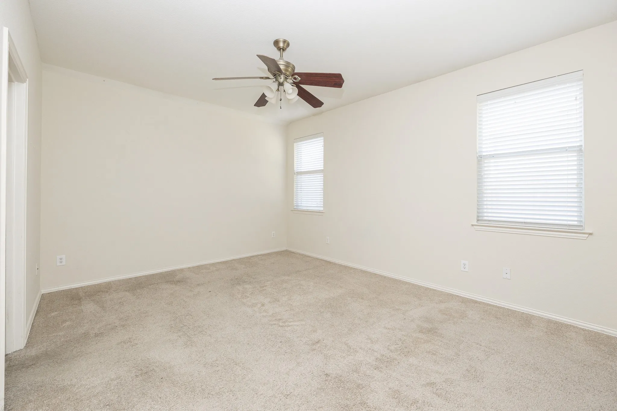 Neutral carpeting, two windows with blinds, and a ceiling fan with light fixture