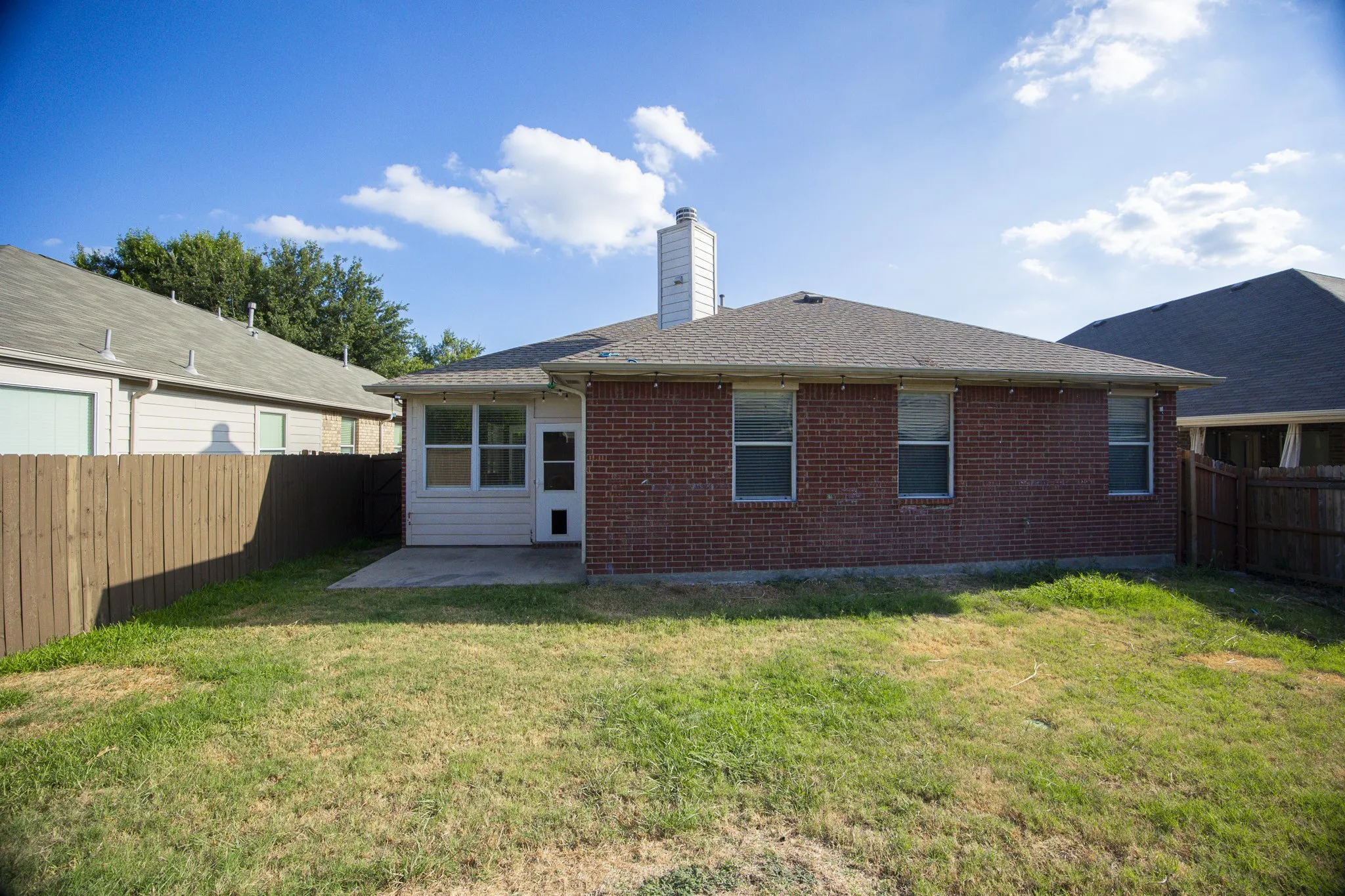 Brick exterior with a screened-in porch, concrete patio, and private wood fencing