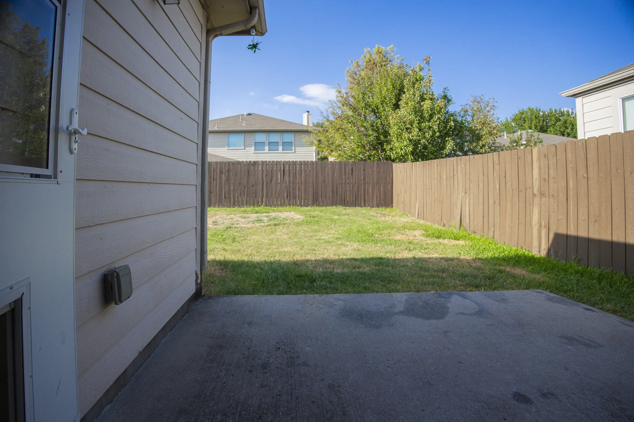Expansive fenced yard featuring a concrete patio, wood privacy fence, and mature trees
