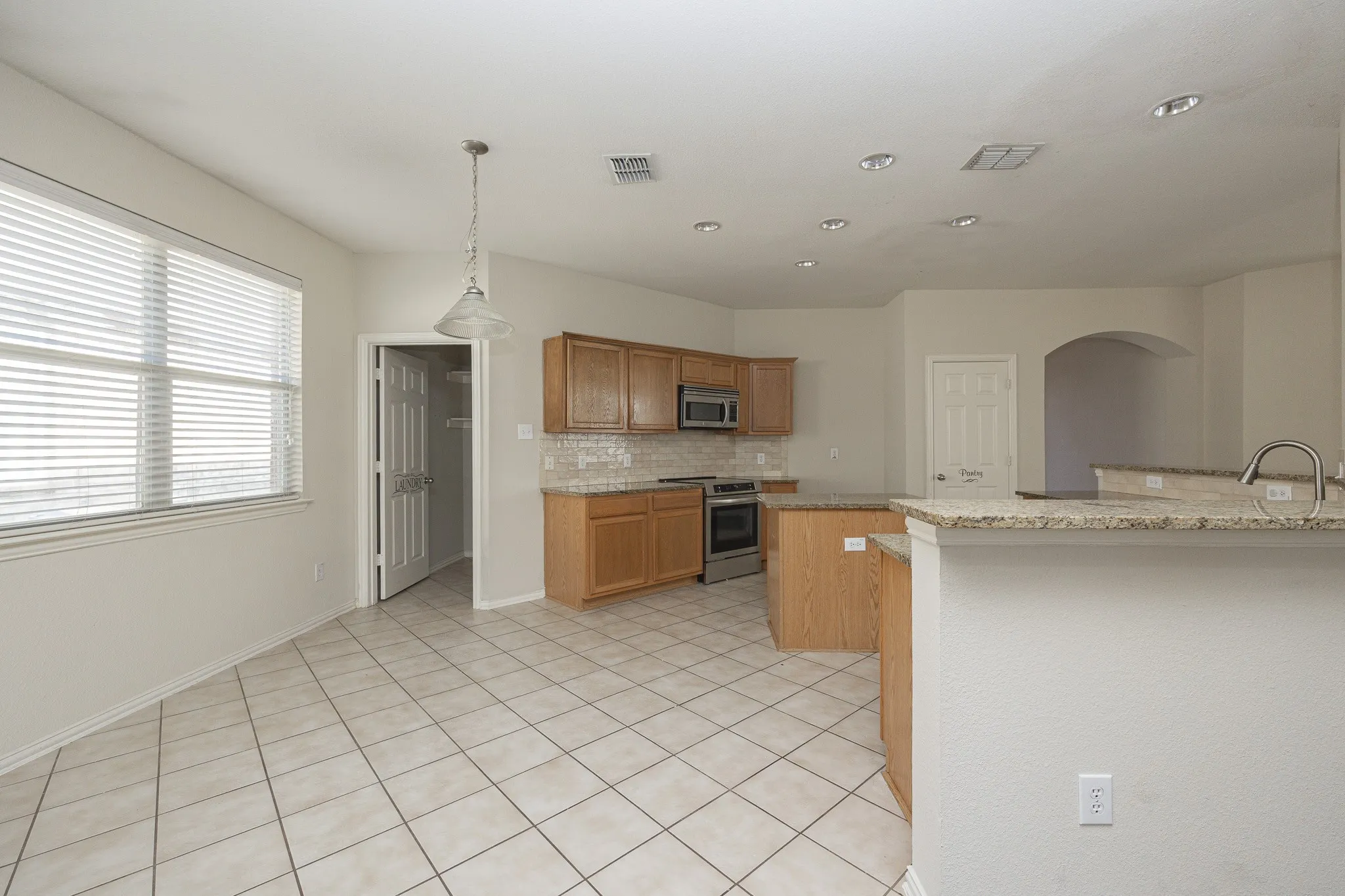 Kitchen featuring wood cabinetry, stainless steel appliances, granite countertops, and tiled flooring