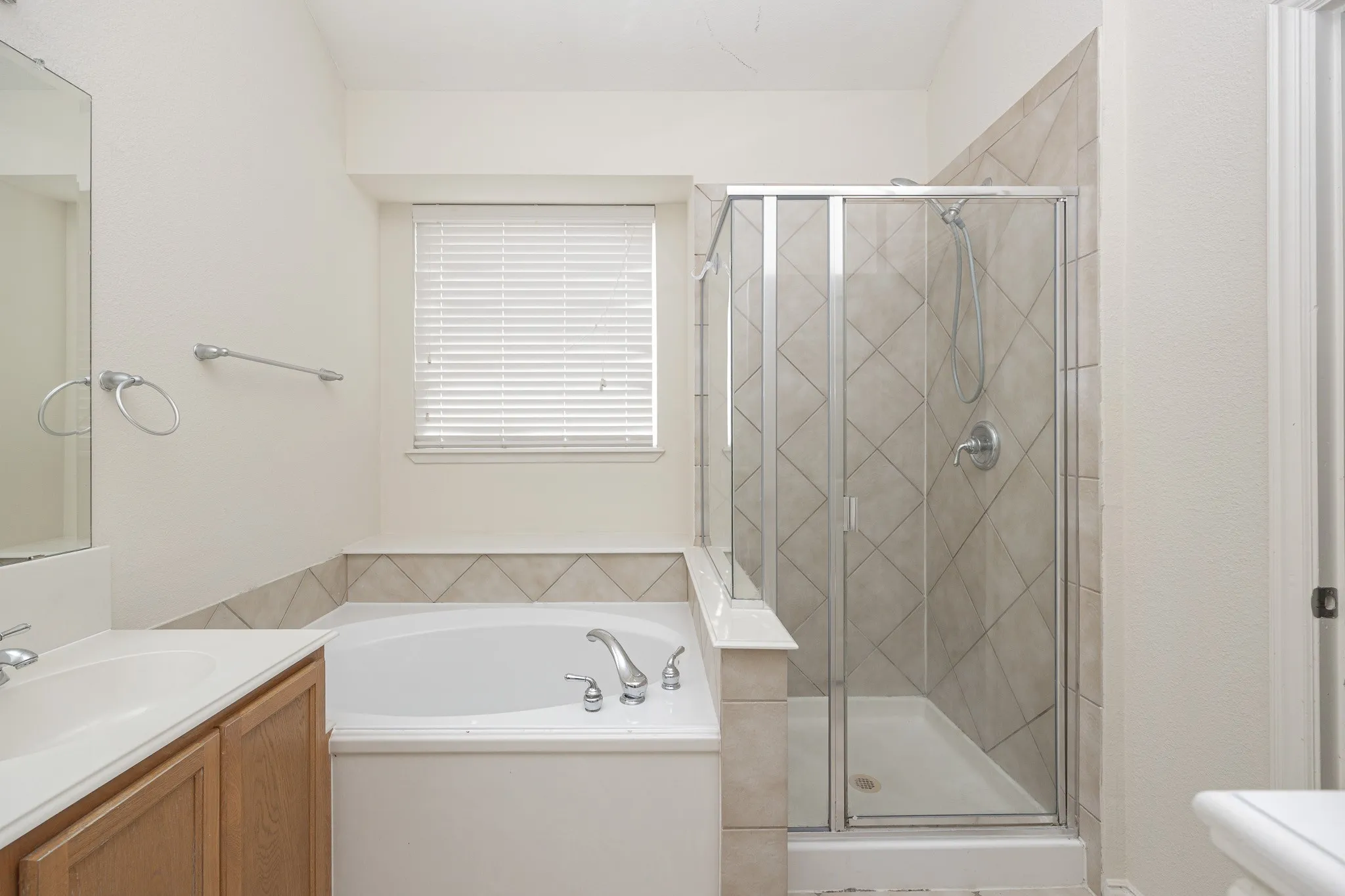 Shower with glass enclosure and tiled surround, soaking tub, vanity with sink, window with blinds