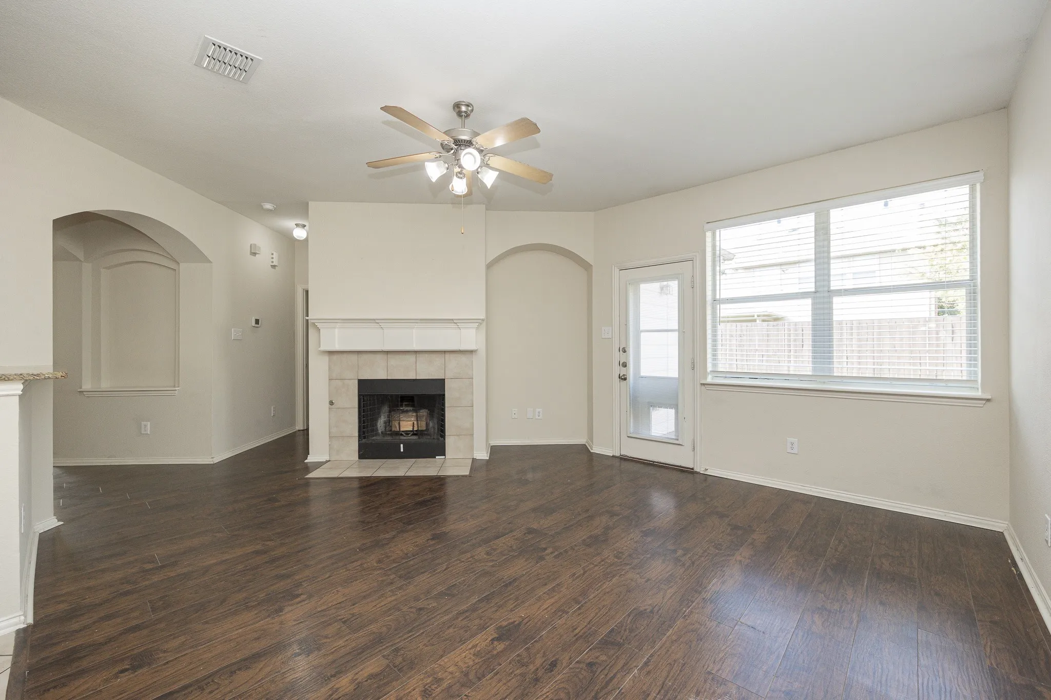 Wood-finish flooring, fireplace with tile surround, ceiling fan, archway detail, and exterior door