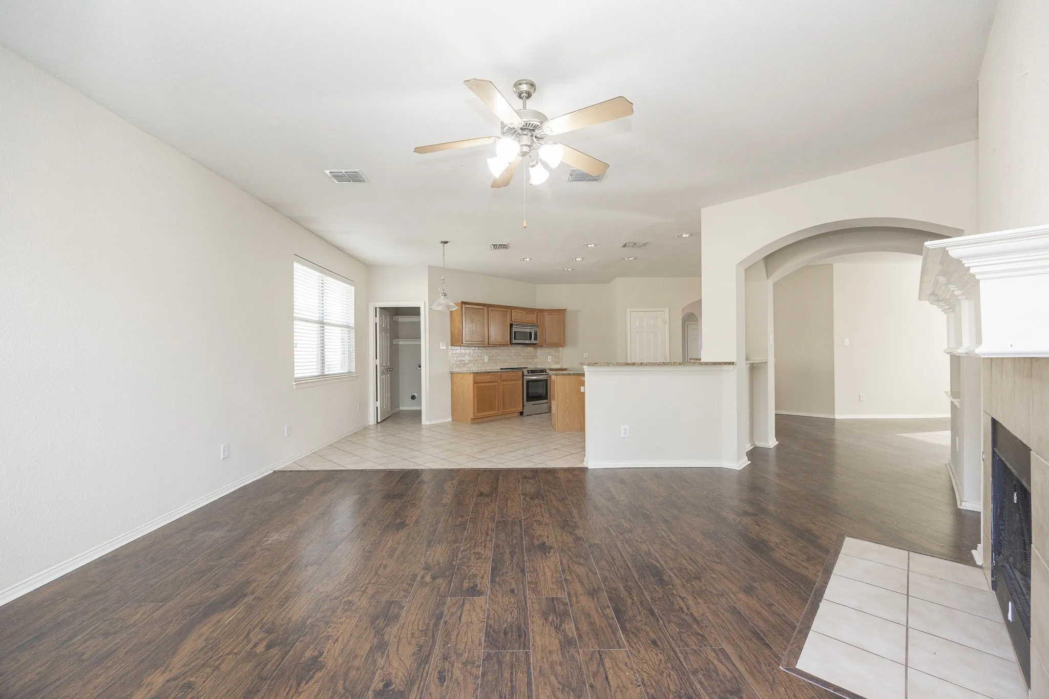 Spacious room featuring wood-finish flooring, a ceiling fan, and a fireplace with a white mantel