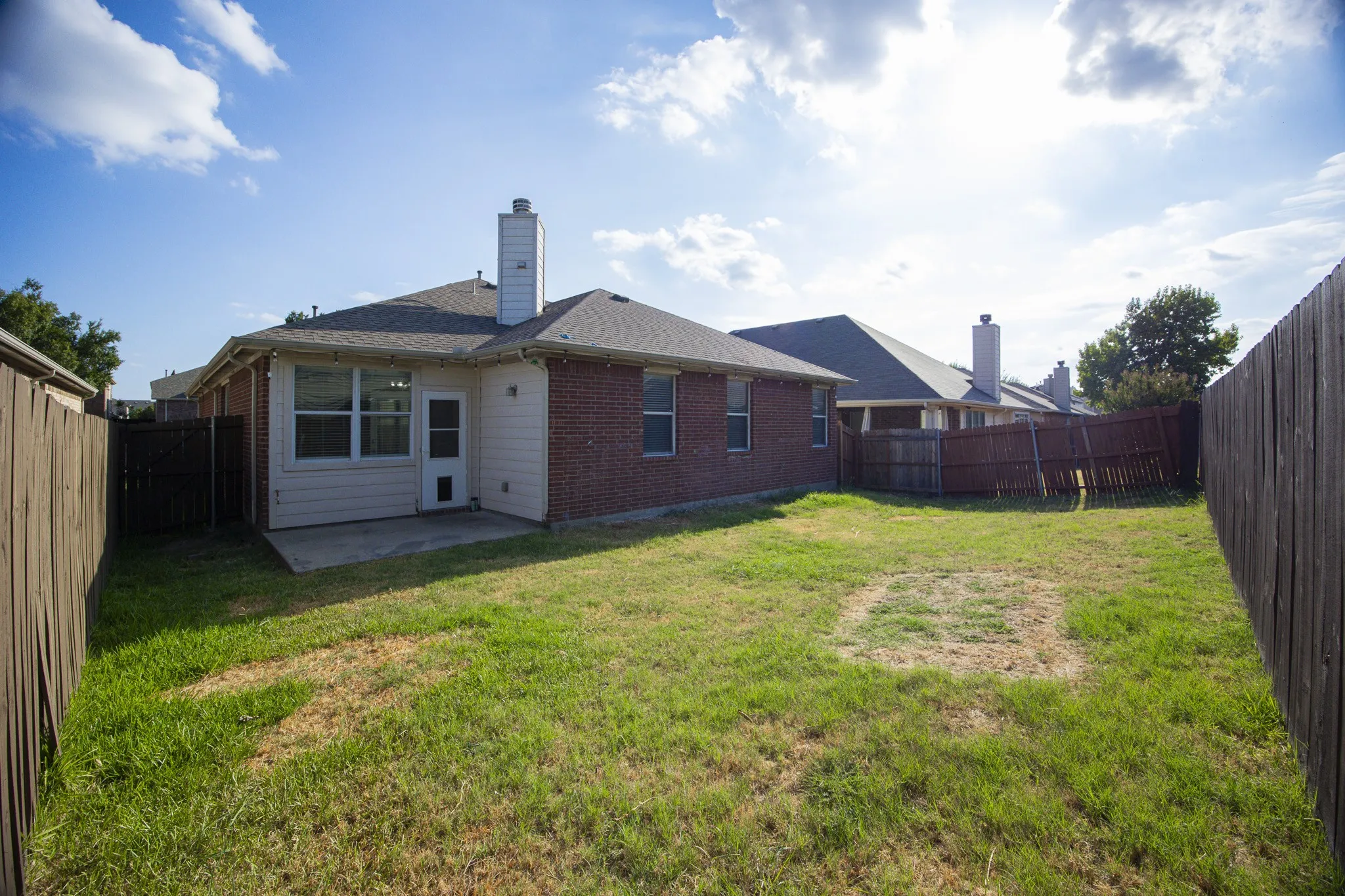 Brick exterior with a white chimney, concrete patio, and fenced backyard