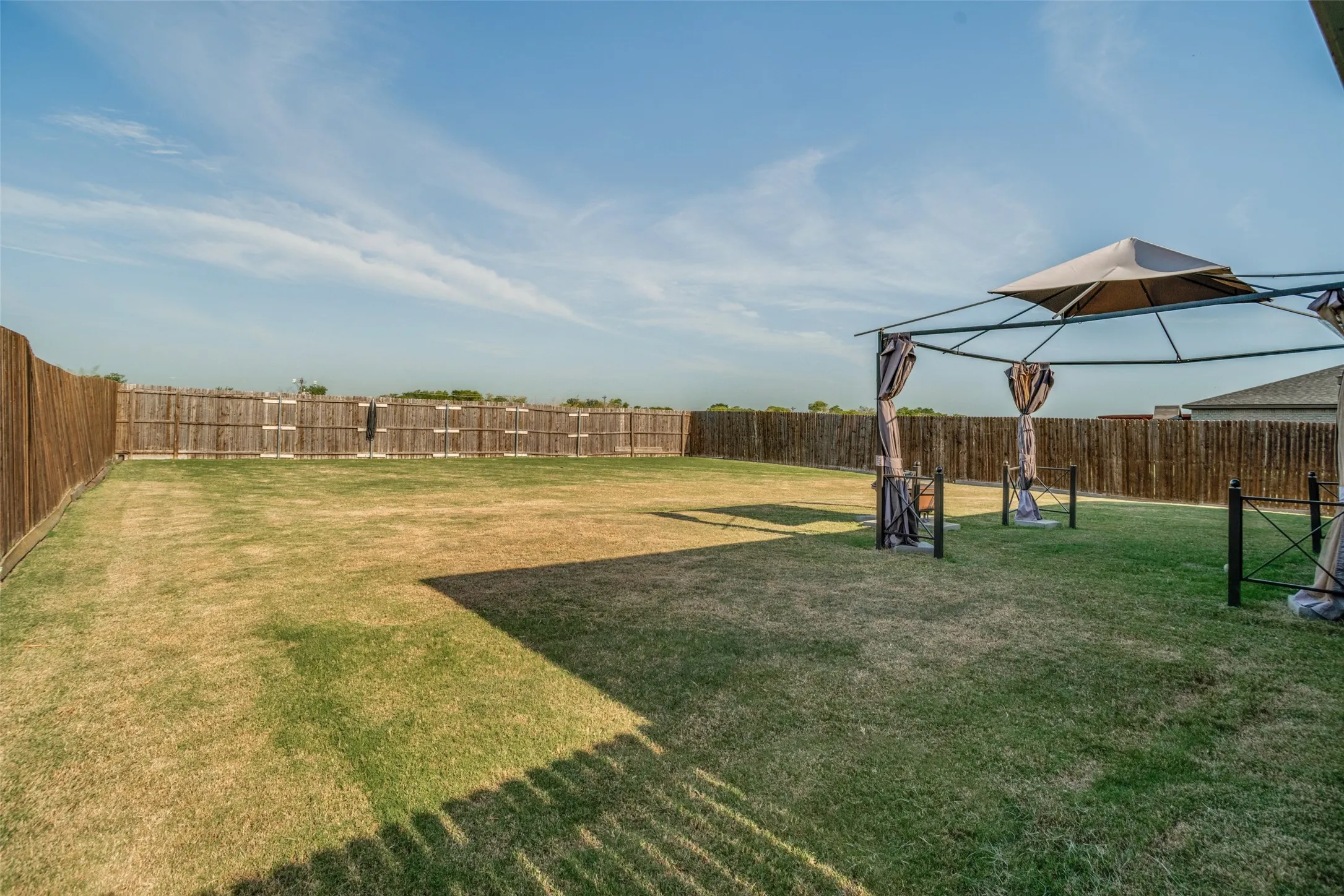 Expansive backyard featuring a privacy fence, large lawn area, and a built-in gazebo structure