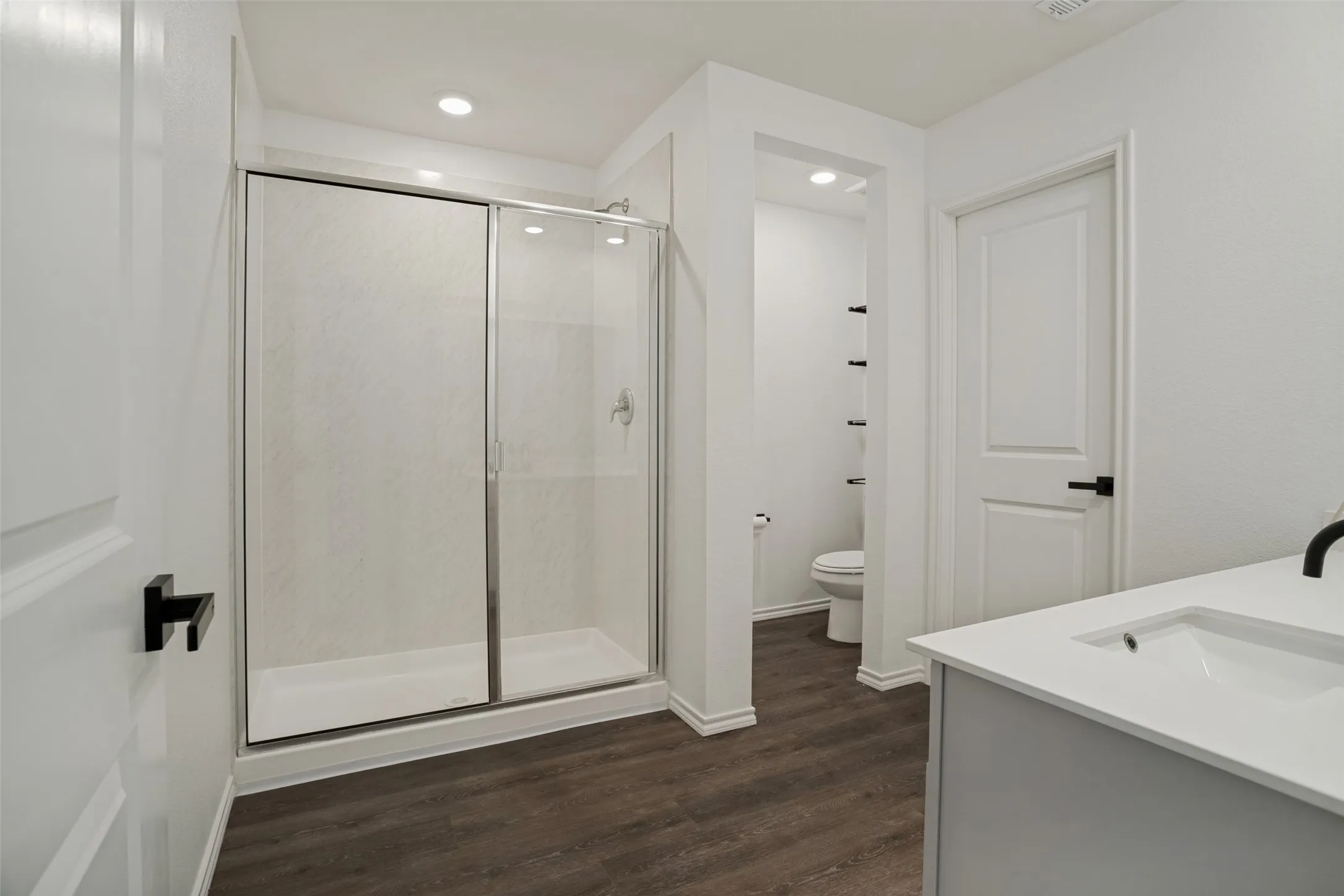 Walk-in shower with sliding glass enclosure, single vanity with integrated sink, wood-finish flooring, and recessed lighting