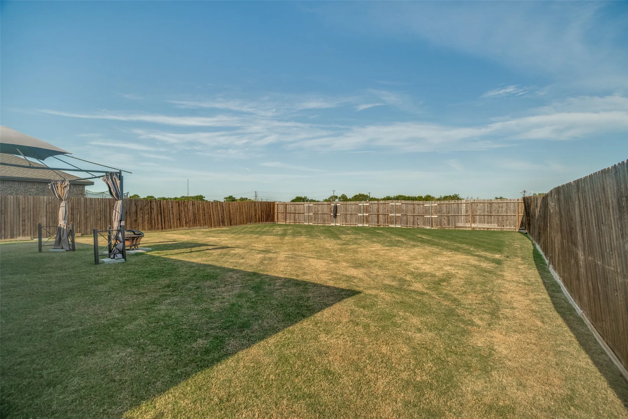 Expansive backyard with a manicured lawn, a large wood privacy fence, and a covered patio structure