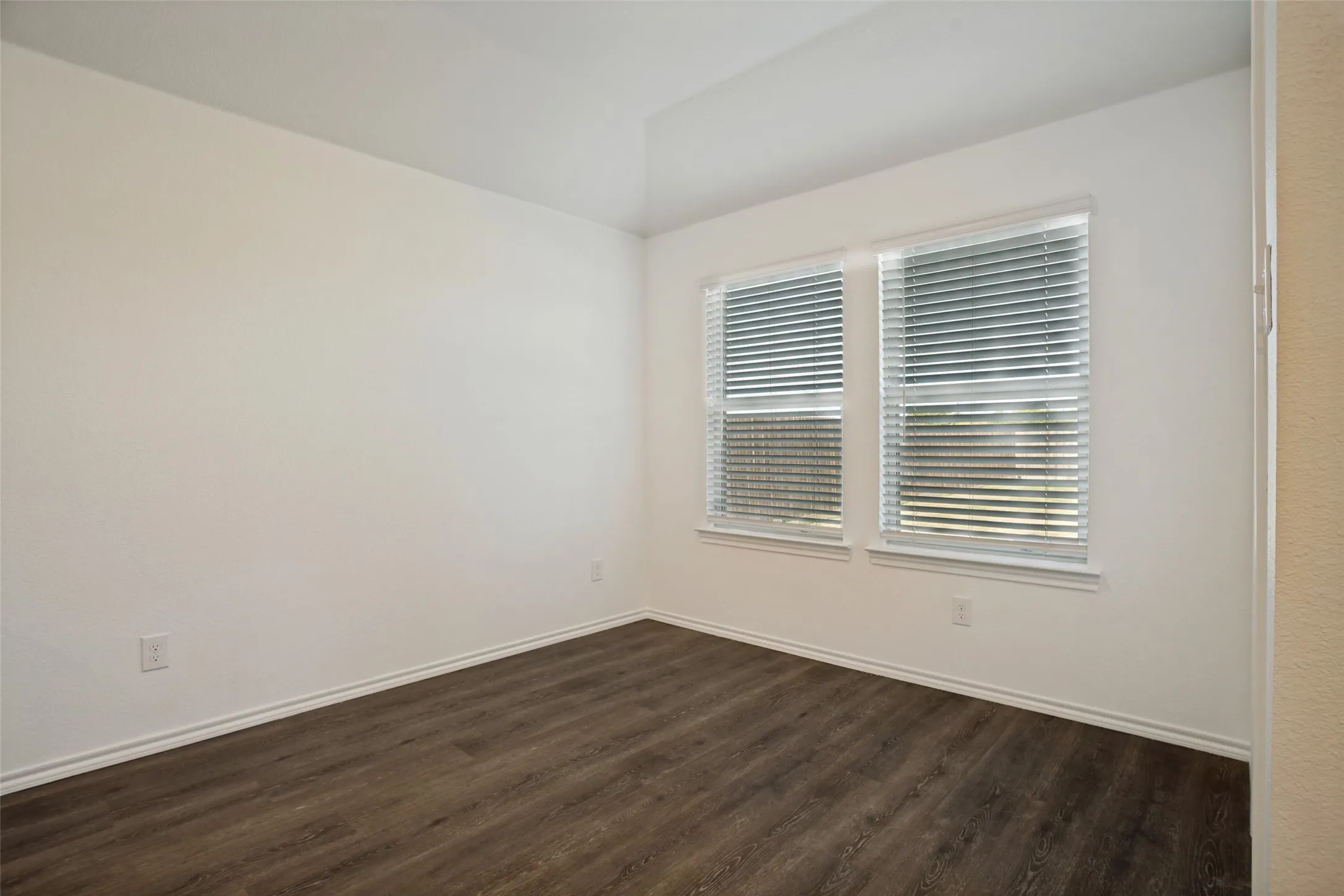 Light-filled room featuring two windows with blinds, wood-finish flooring, and neutral wall paint