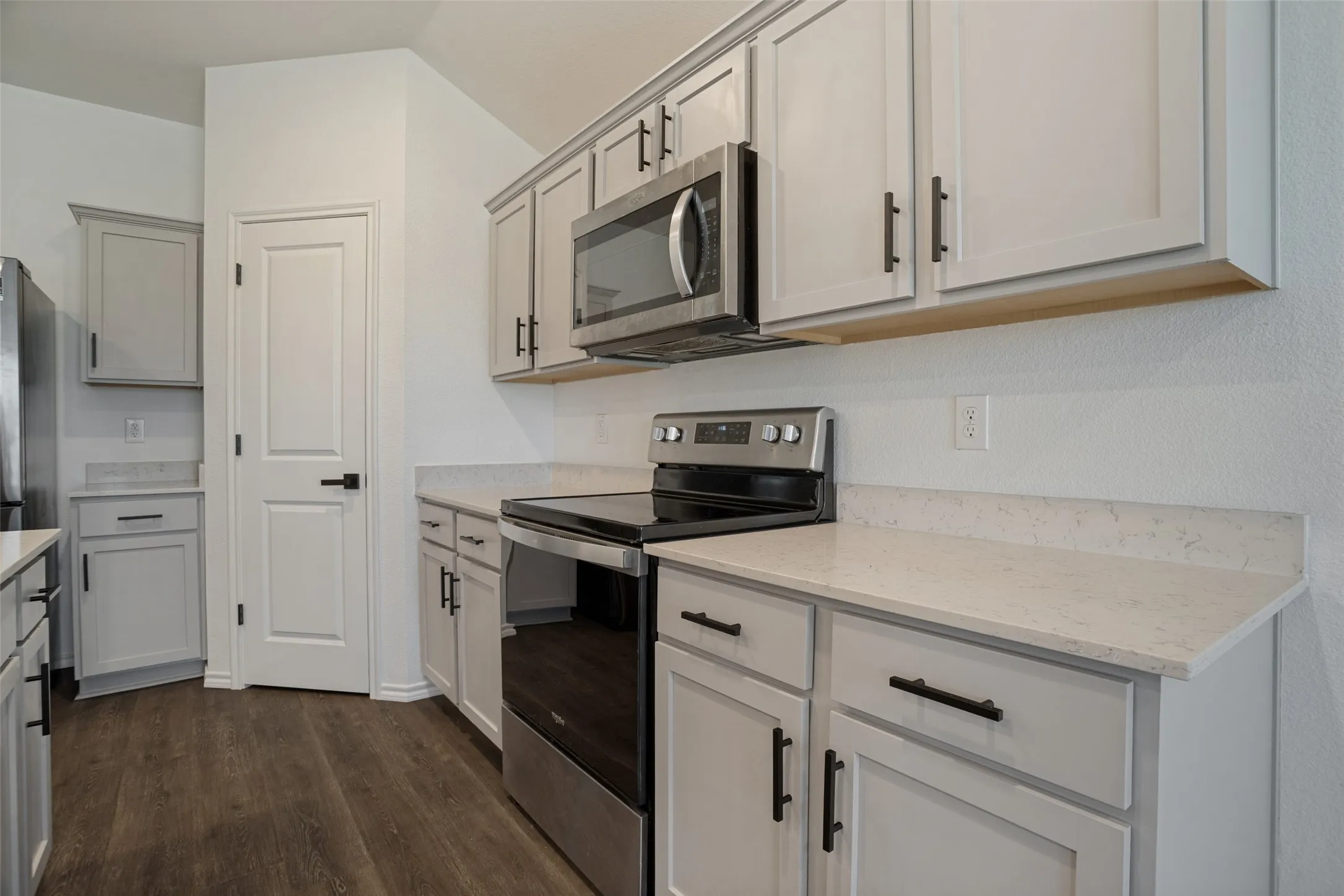 Contemporary kitchen featuring light-toned cabinetry with matte black hardware, stainless steel appliances, wood-finish flooring, and light-toned countertops