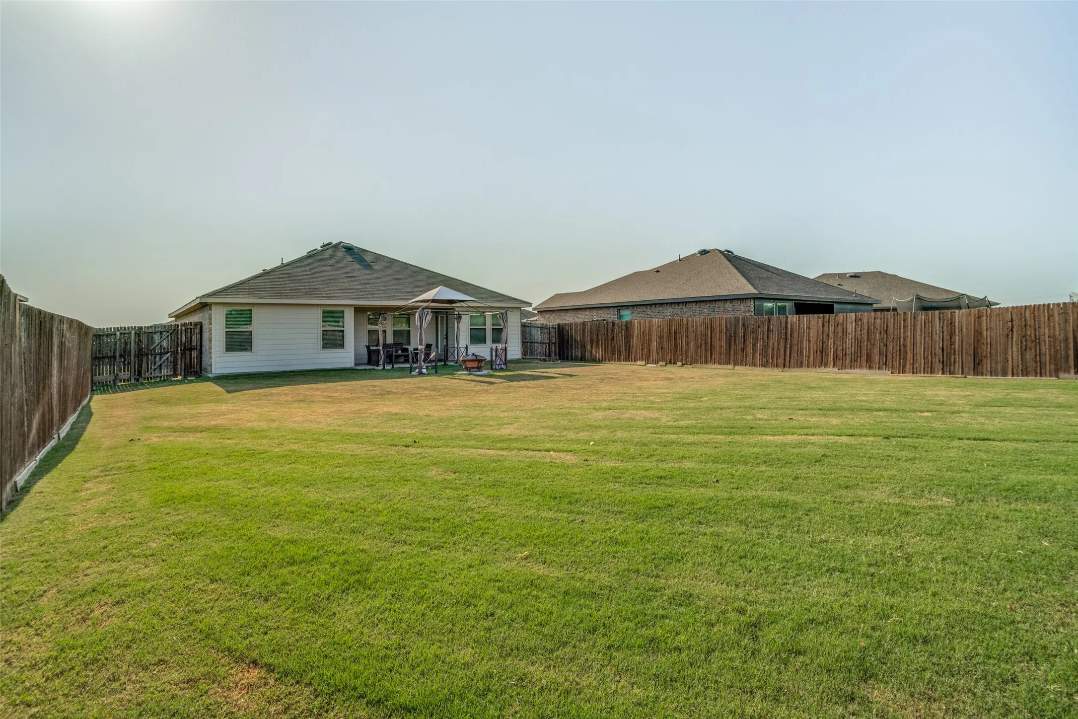 Expansive grass lawn with a wood plank privacy fence and a one-story dwelling featuring a gabled roof and covered patio