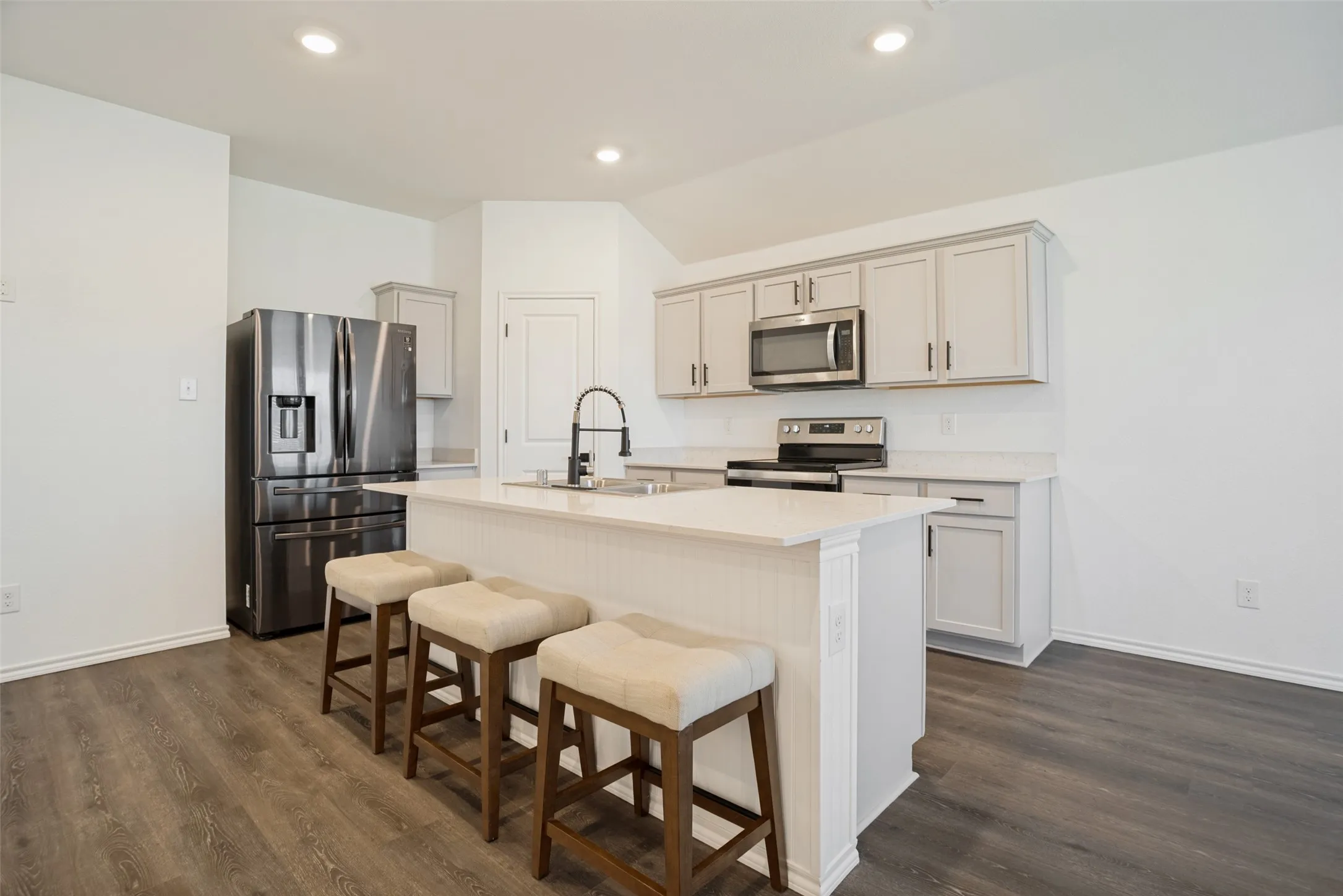 Kitchen with a center island, light-toned cabinetry, stainless steel appliances, and wood-finish flooring
