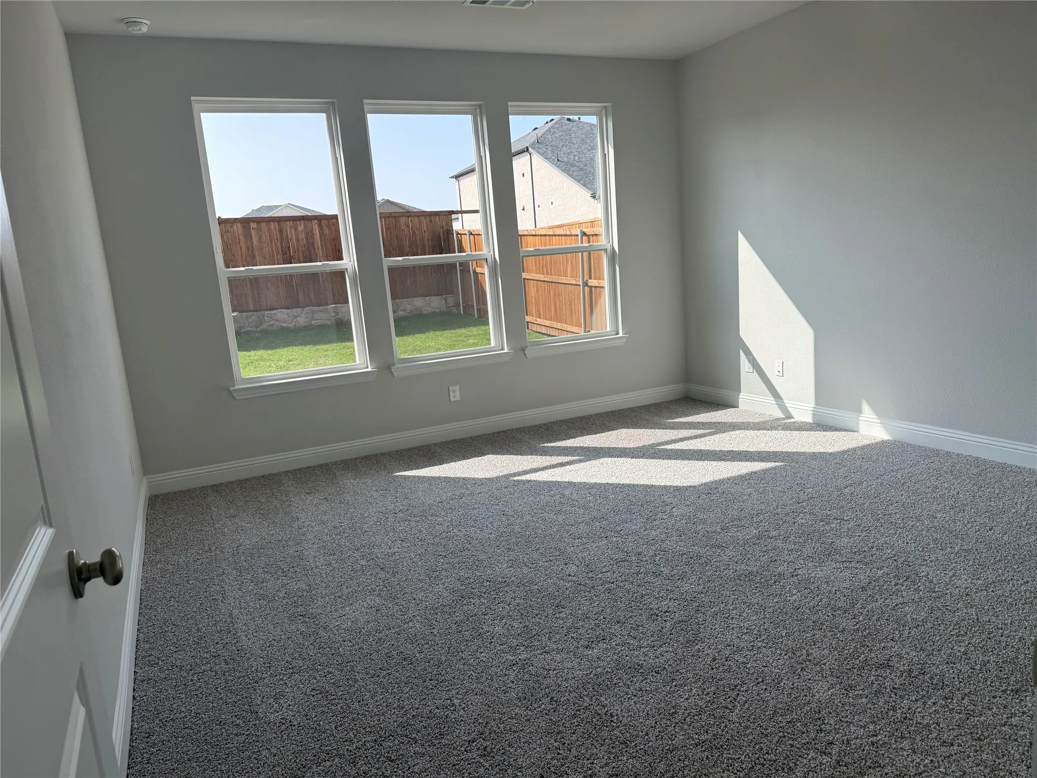 Three large windows, fresh gray carpeting, and neutral wall tones