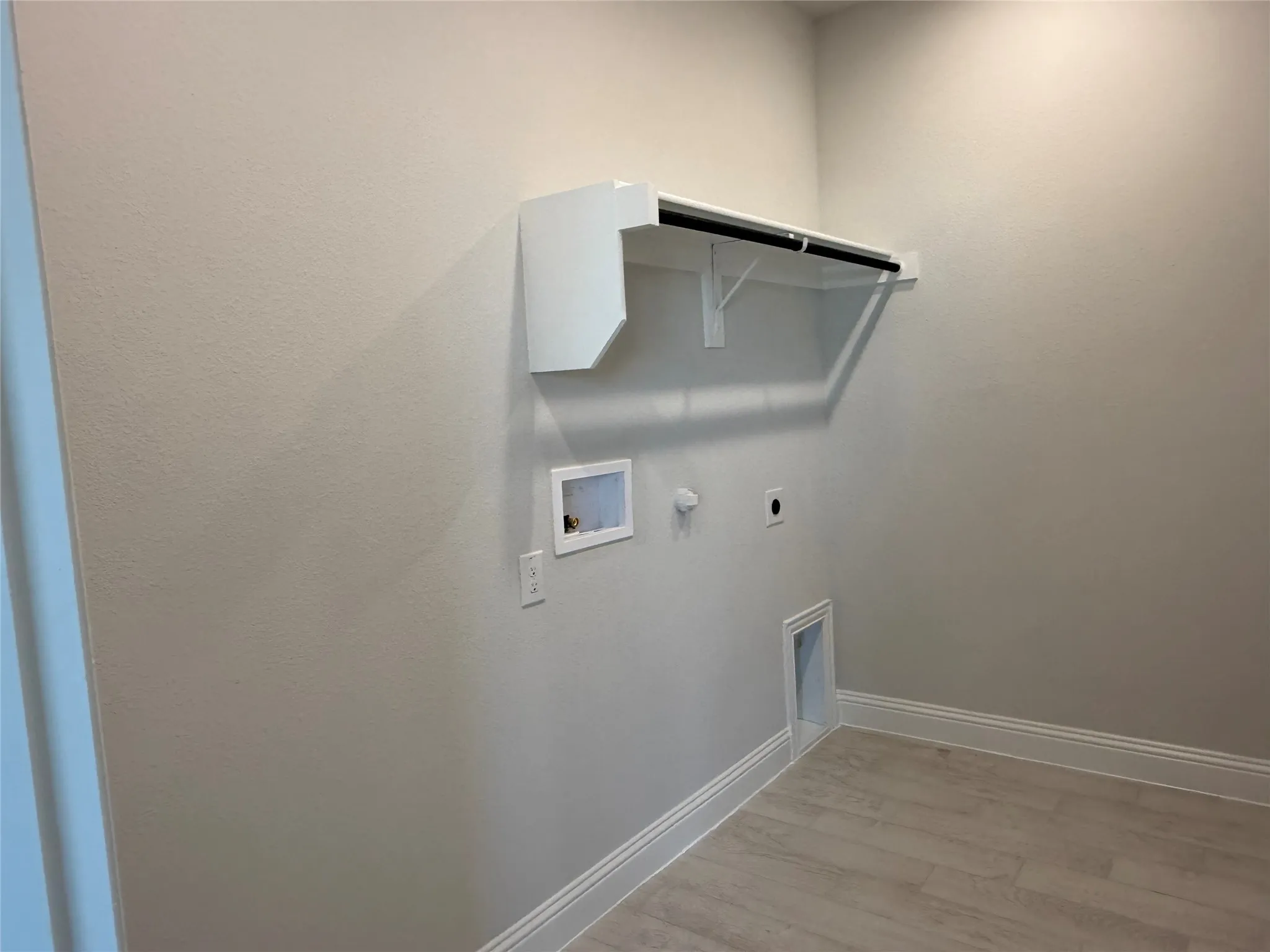 Utility room featuring a wall-mounted shelf with hanging rod, wood-finish flooring, and white baseboards