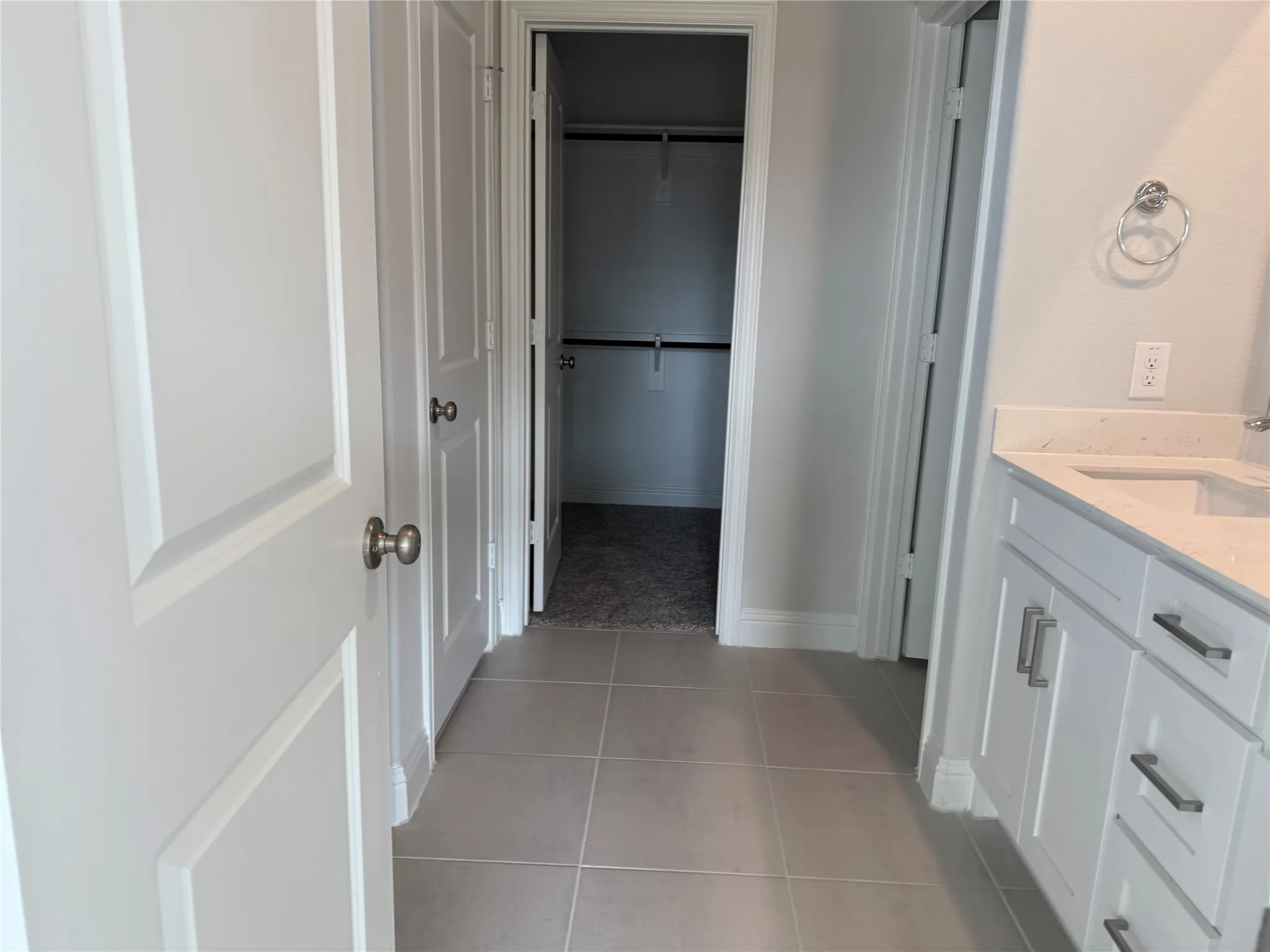 White paneled doors, light gray tile flooring, white vanity with integrated sink, light countertop, and brushed nickel hardware
